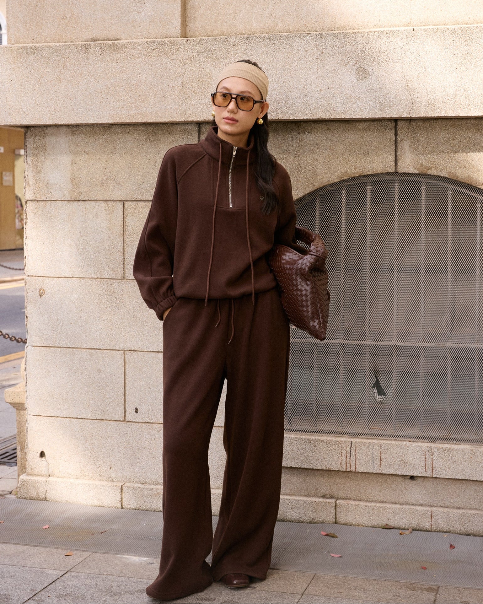 woman wearing a brown outfit standing against a stone wall.