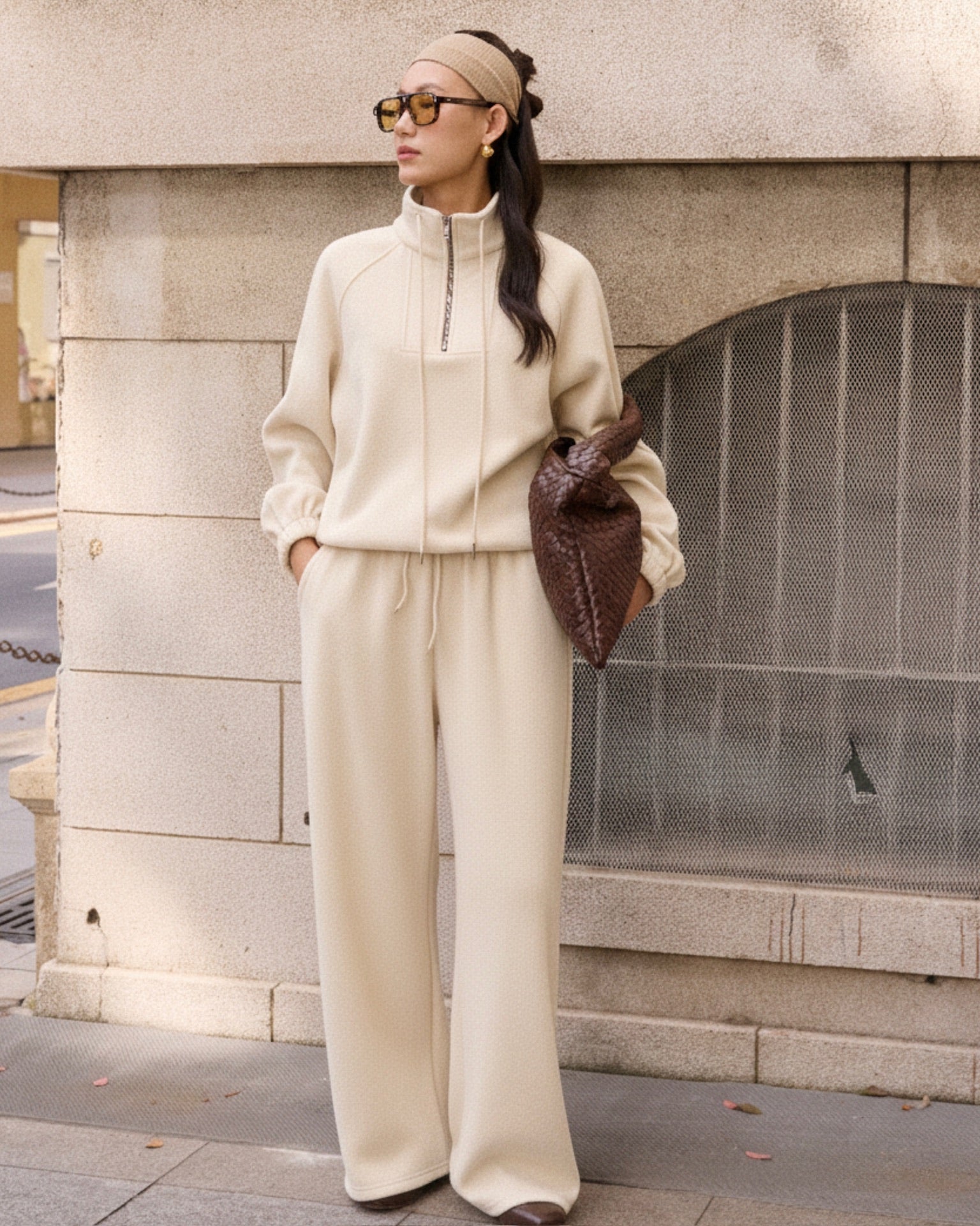 woman wearing a beige tracksuit standing against a stone wall.