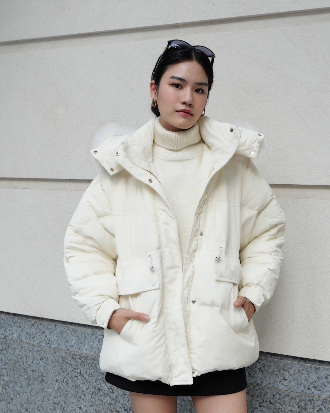 woman wearing a white puffer jacket and black skirt against a plain background
