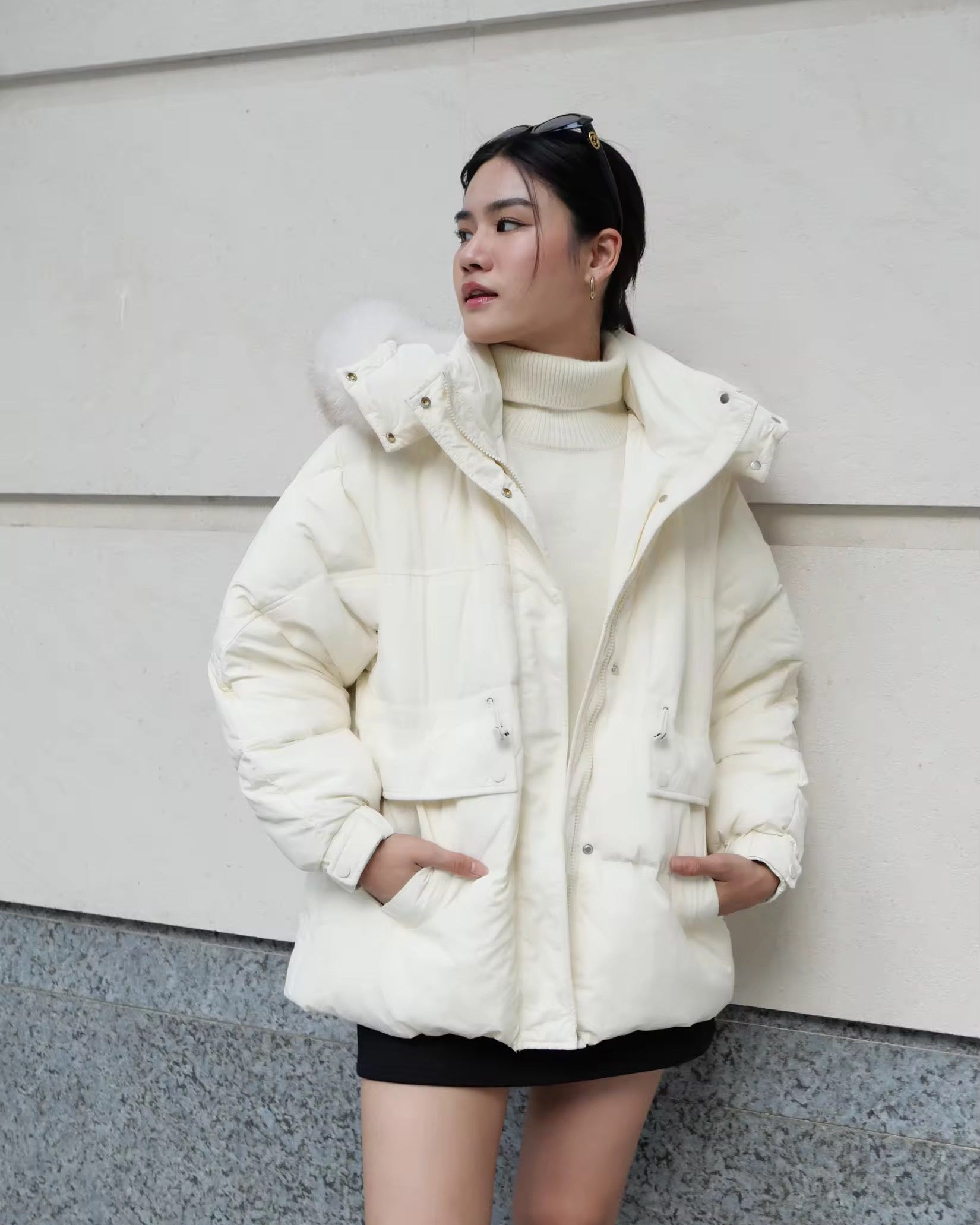 woman wearing a white puffer jacket in front of a light-colored wall.