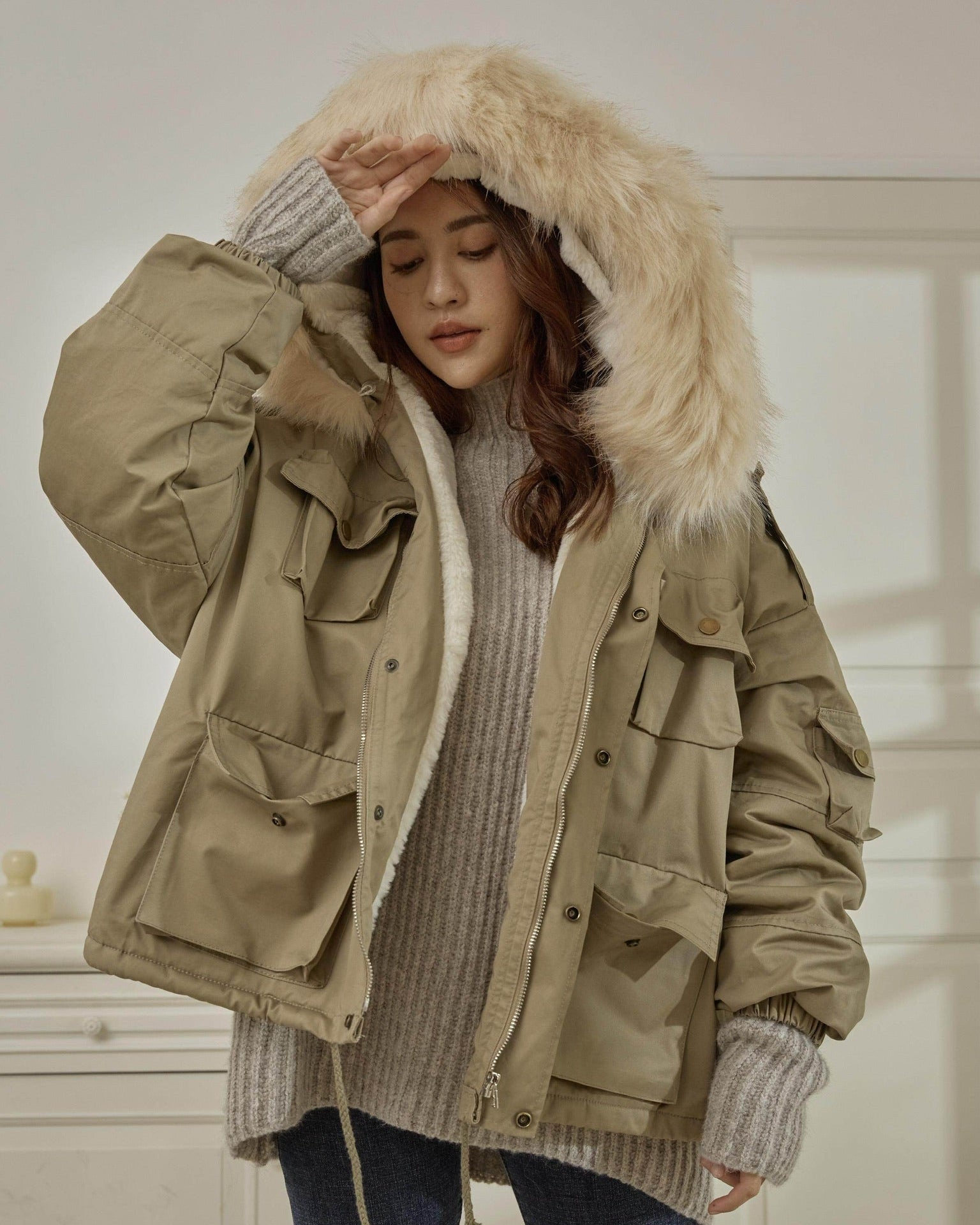 woman wearing a beige parka with a fur-lined hood indoors
