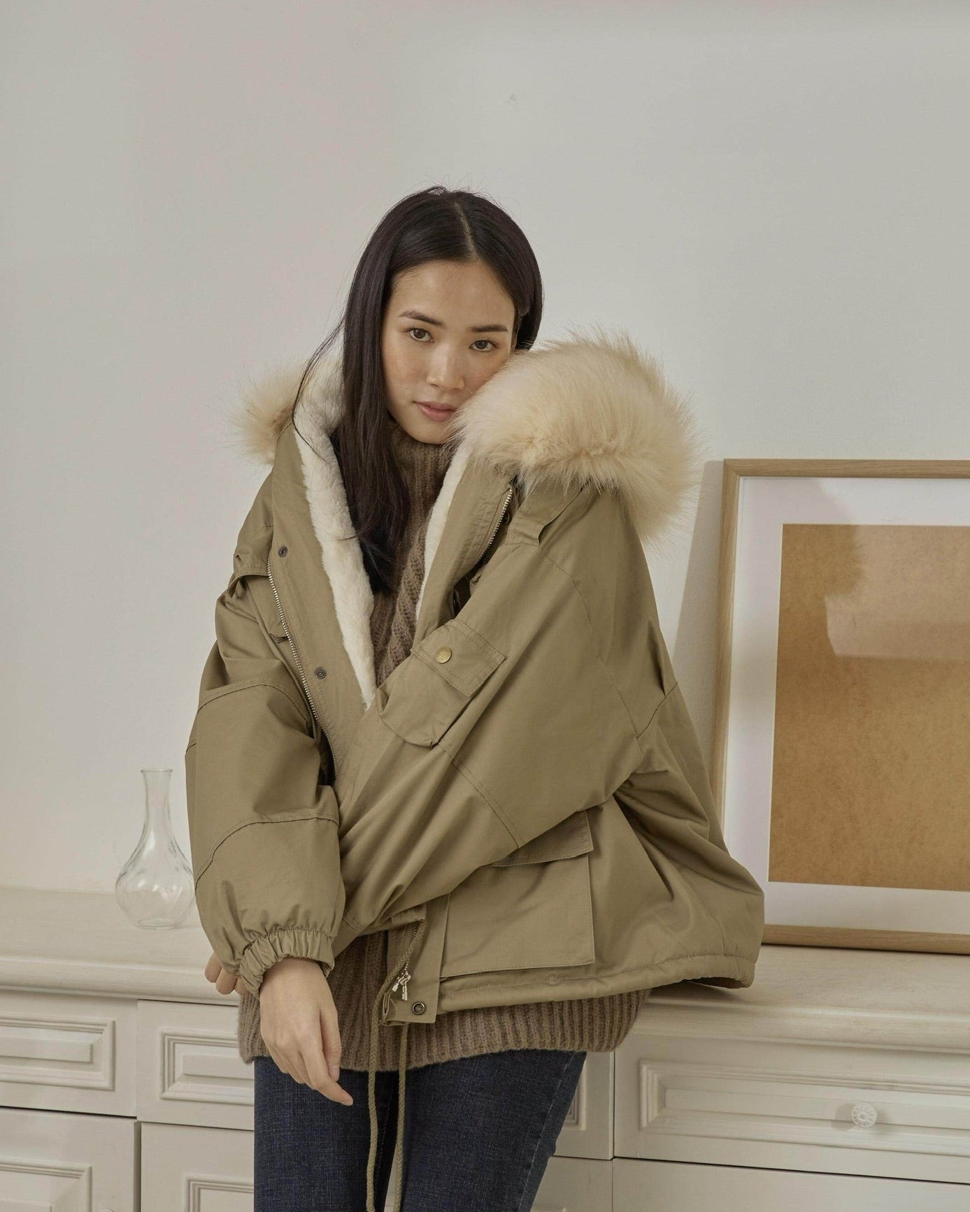 Woman wearing a beige parka with fur hood in an indoor setting
