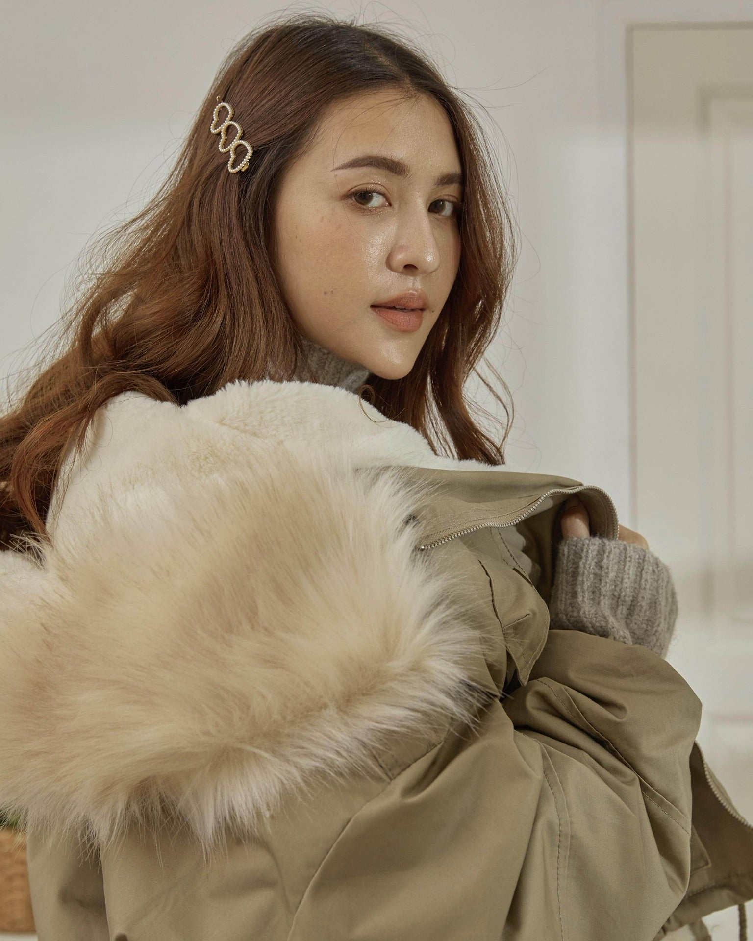 Woman wearing a beige coat with fur trim indoors