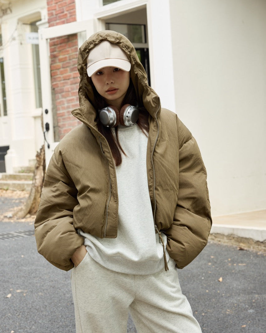woman wearing a brown puffer jacket and white pants standing on a street.