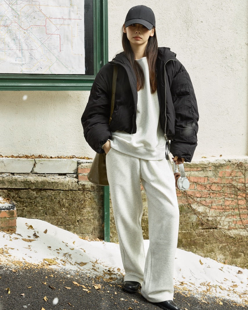 woman wearing a black jacket and white pants standing outdoors against a building.