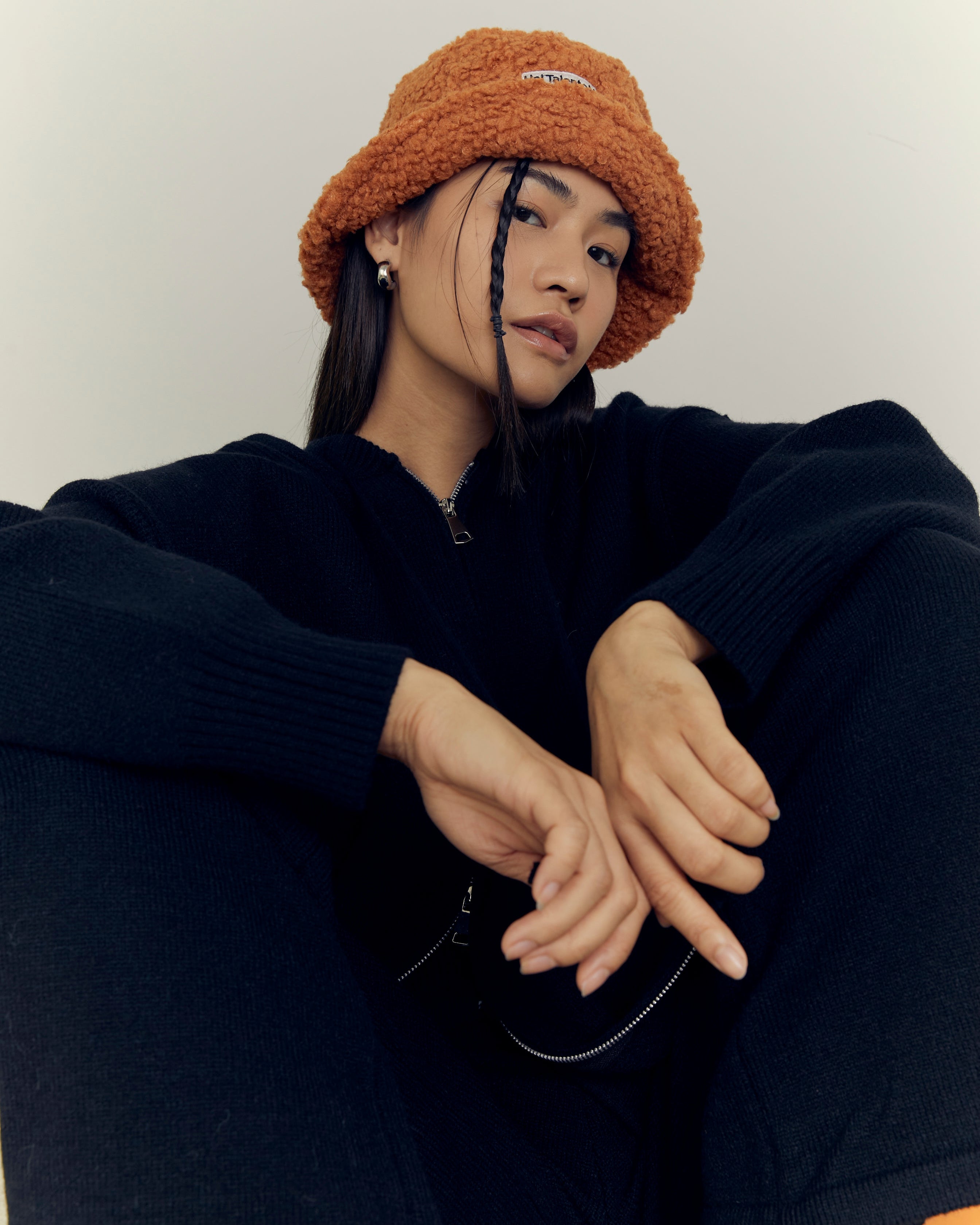 woman wearing a brown beanie and black outfit sitting against a white background