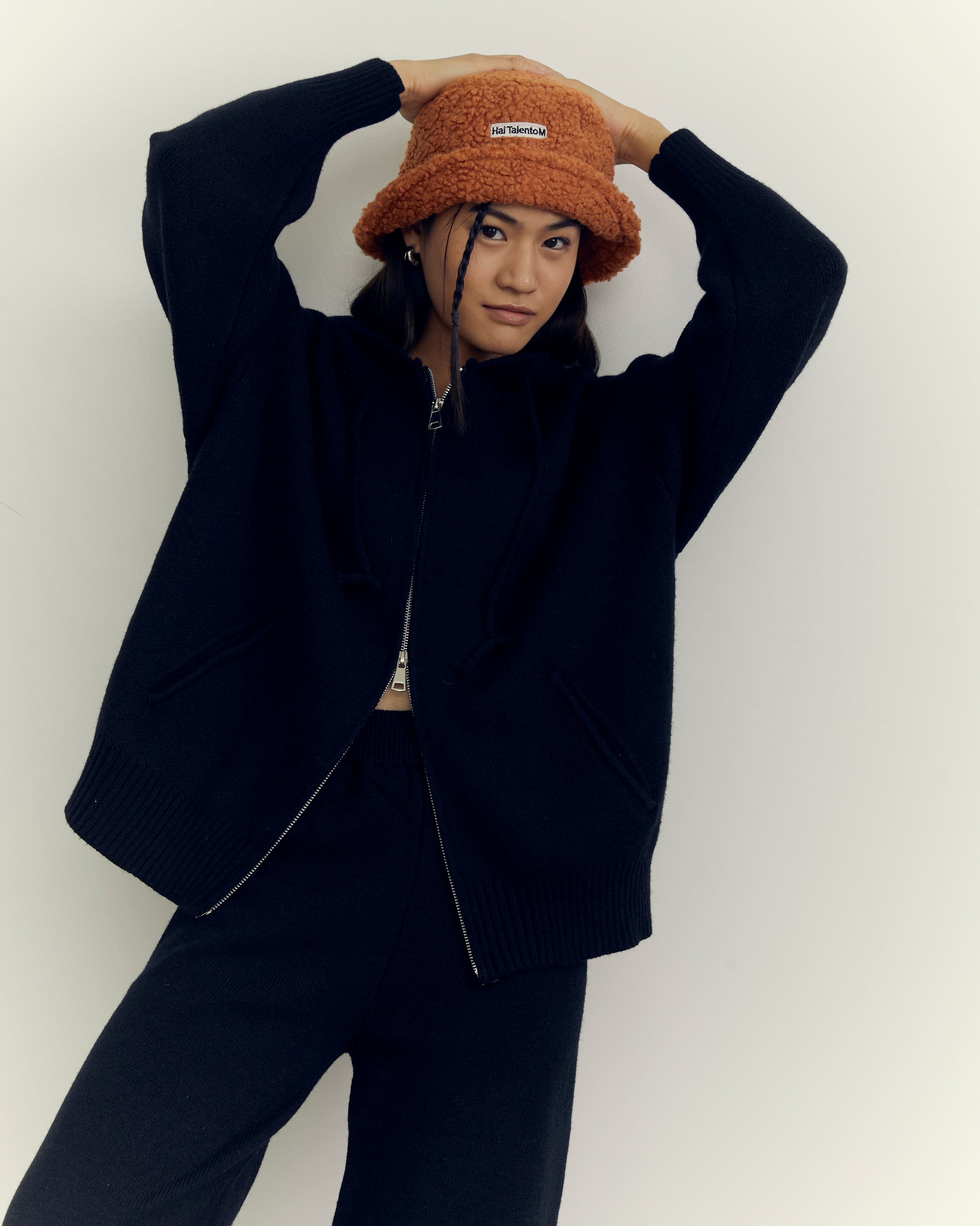 woman wearing a black outfit and orange beanie against a white background