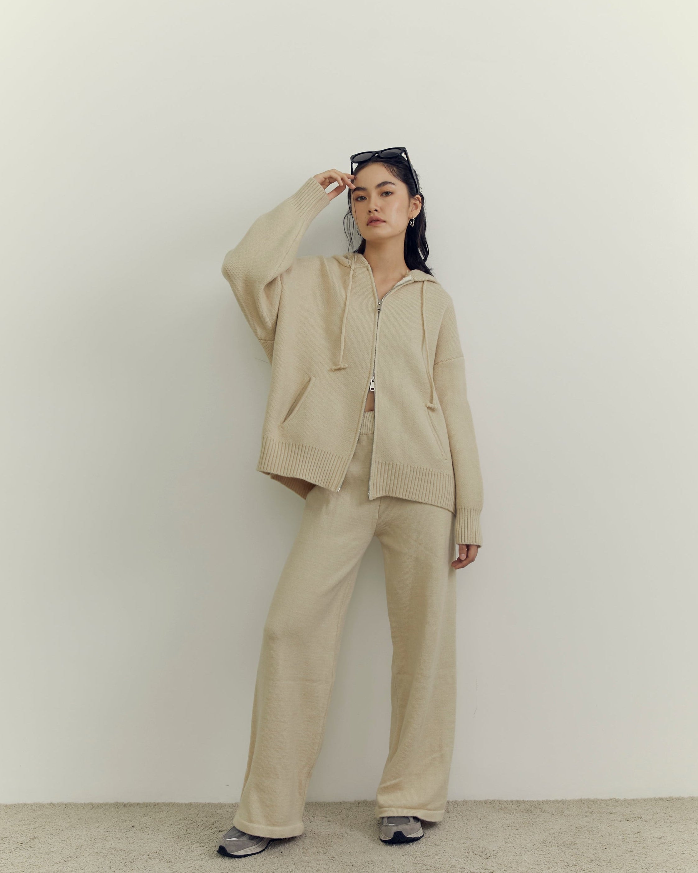 woman wearing a beige suit standing against a plain white wall.