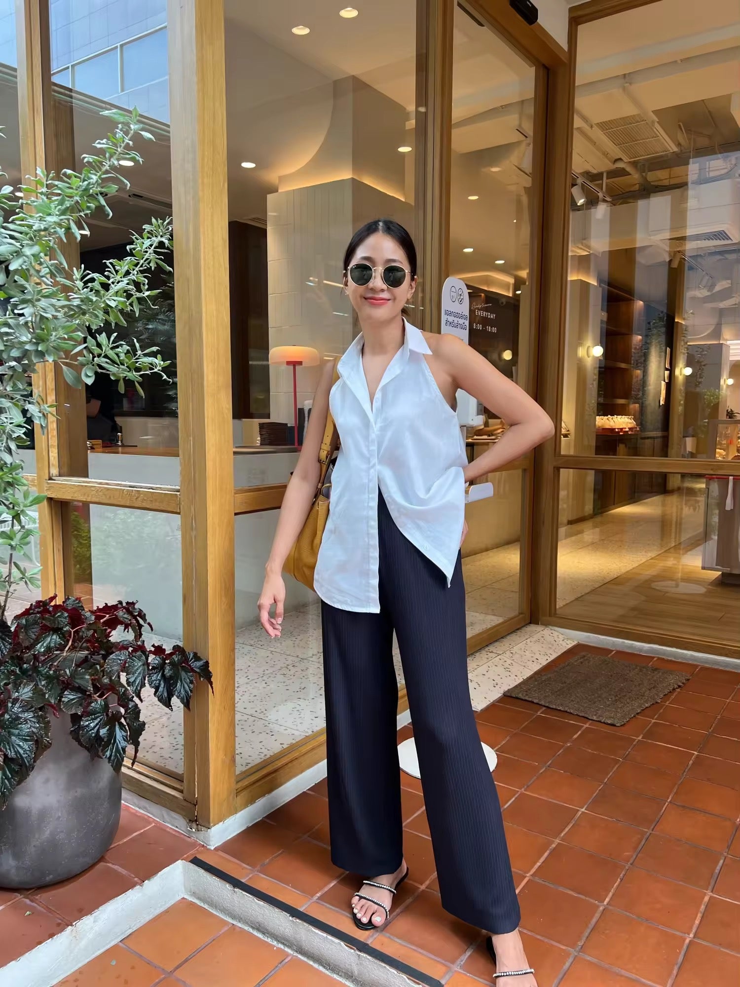 Woman in a white blouse and black pants standing in front of a glass door entrance.