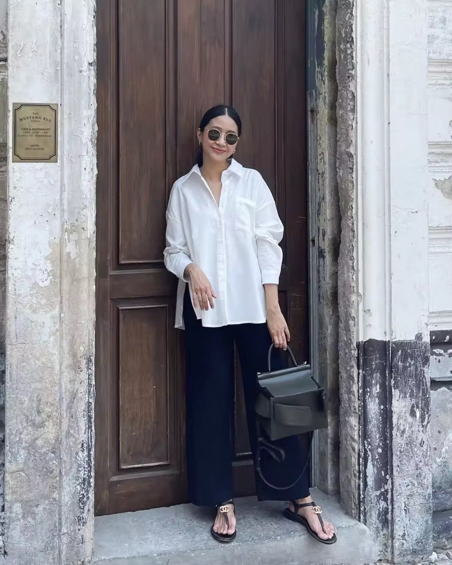 Woman in a white shirt and dark pants standing in front of a wooden door.