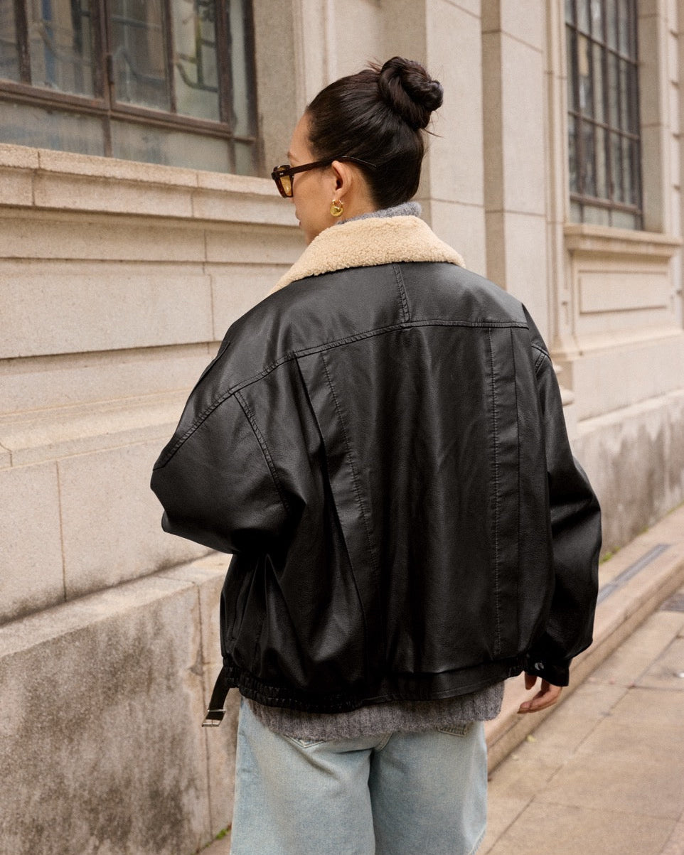 woman wearing a black leather jacket with a beige fur collar, standing on steps.
