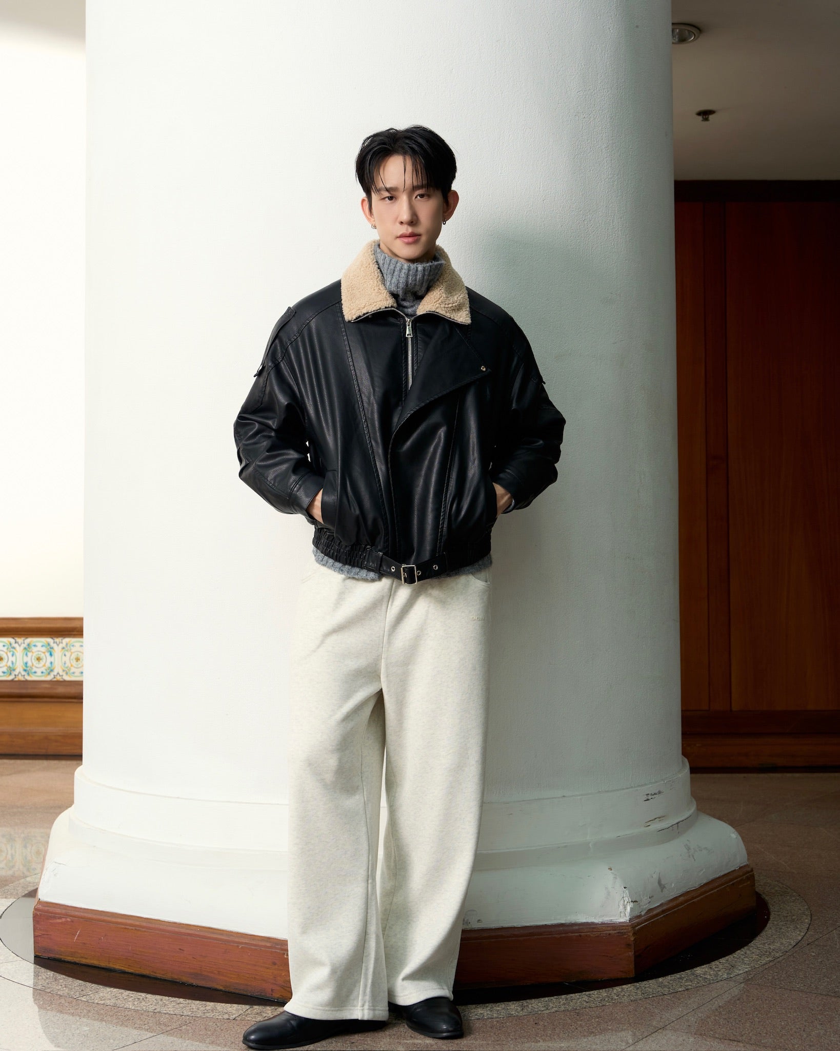 Man wearing a black leather jacket with a white interior, standing against a white column.