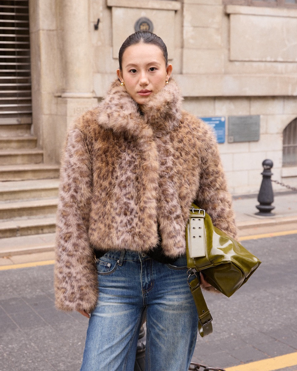 woman wearing a fur coat and jeans with a green bag on a street.