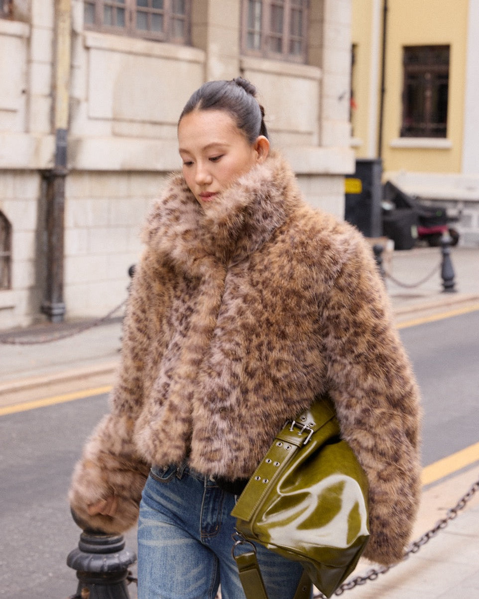 Woman wearing a fur coat and holding a green bag on a city street.
