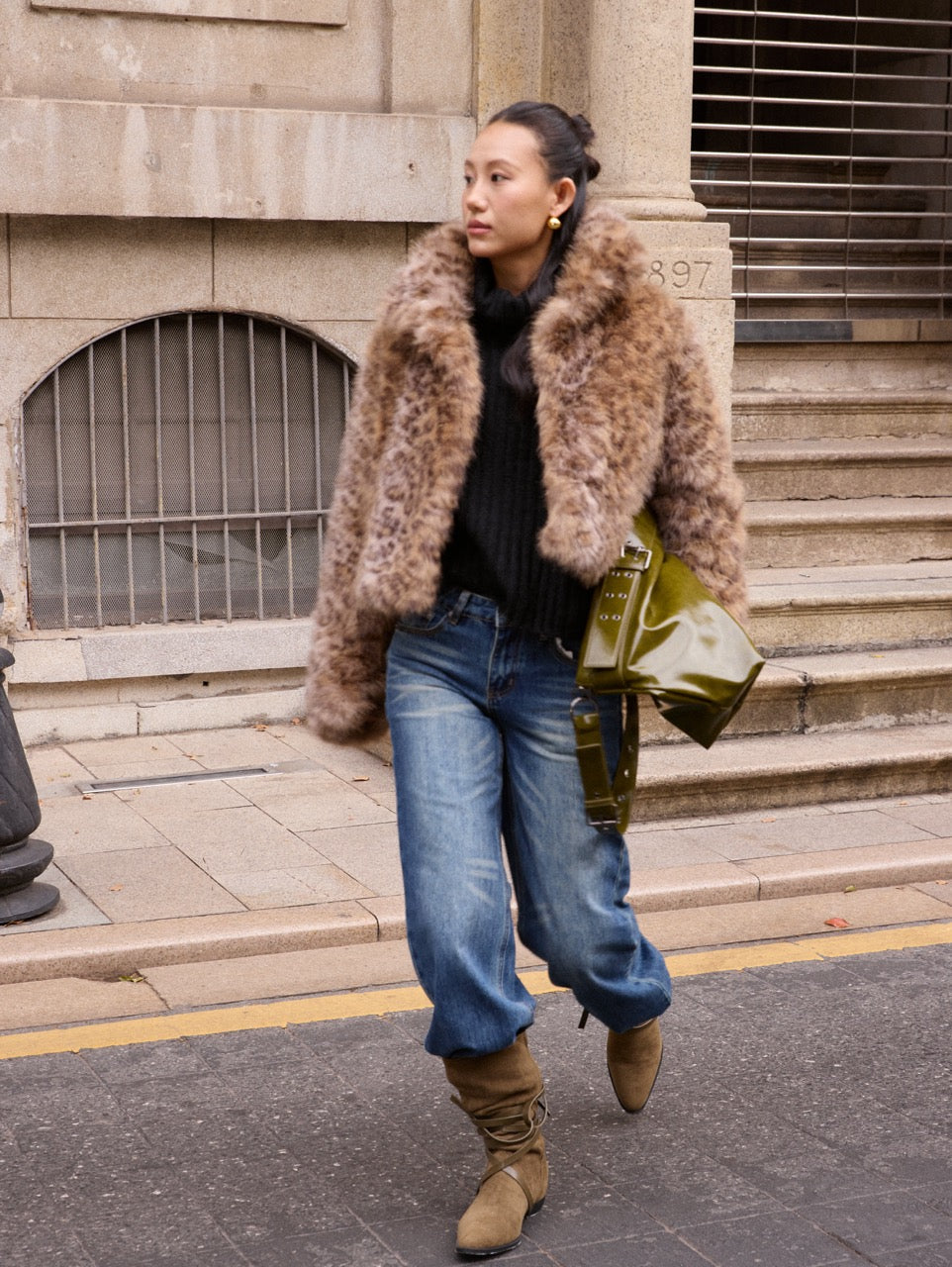 Woman wearing a fur coat and jeans standing on steps outside a building.