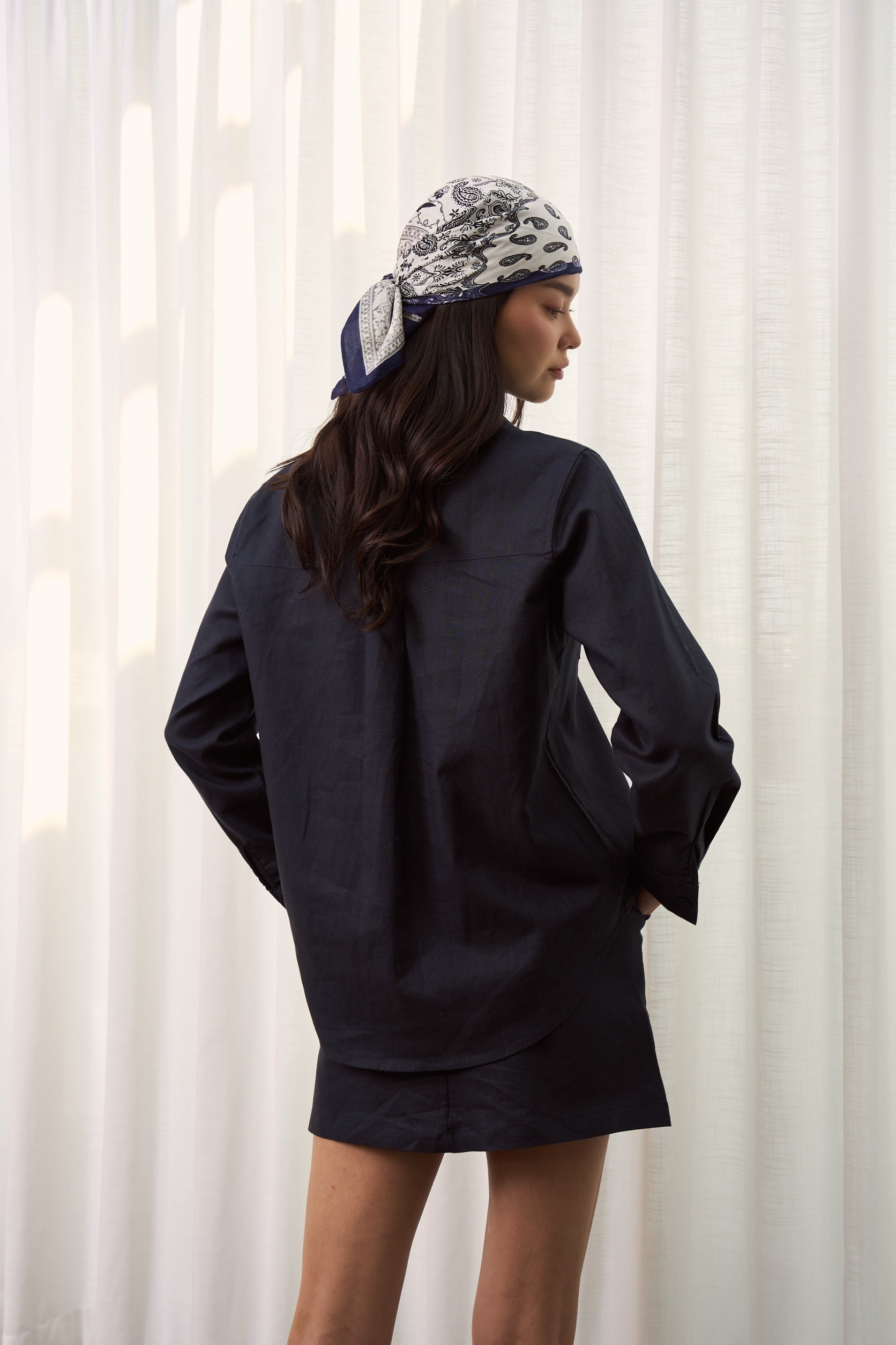 Back of a woman wearing a dark navy linen shirt with linen skirt looking back