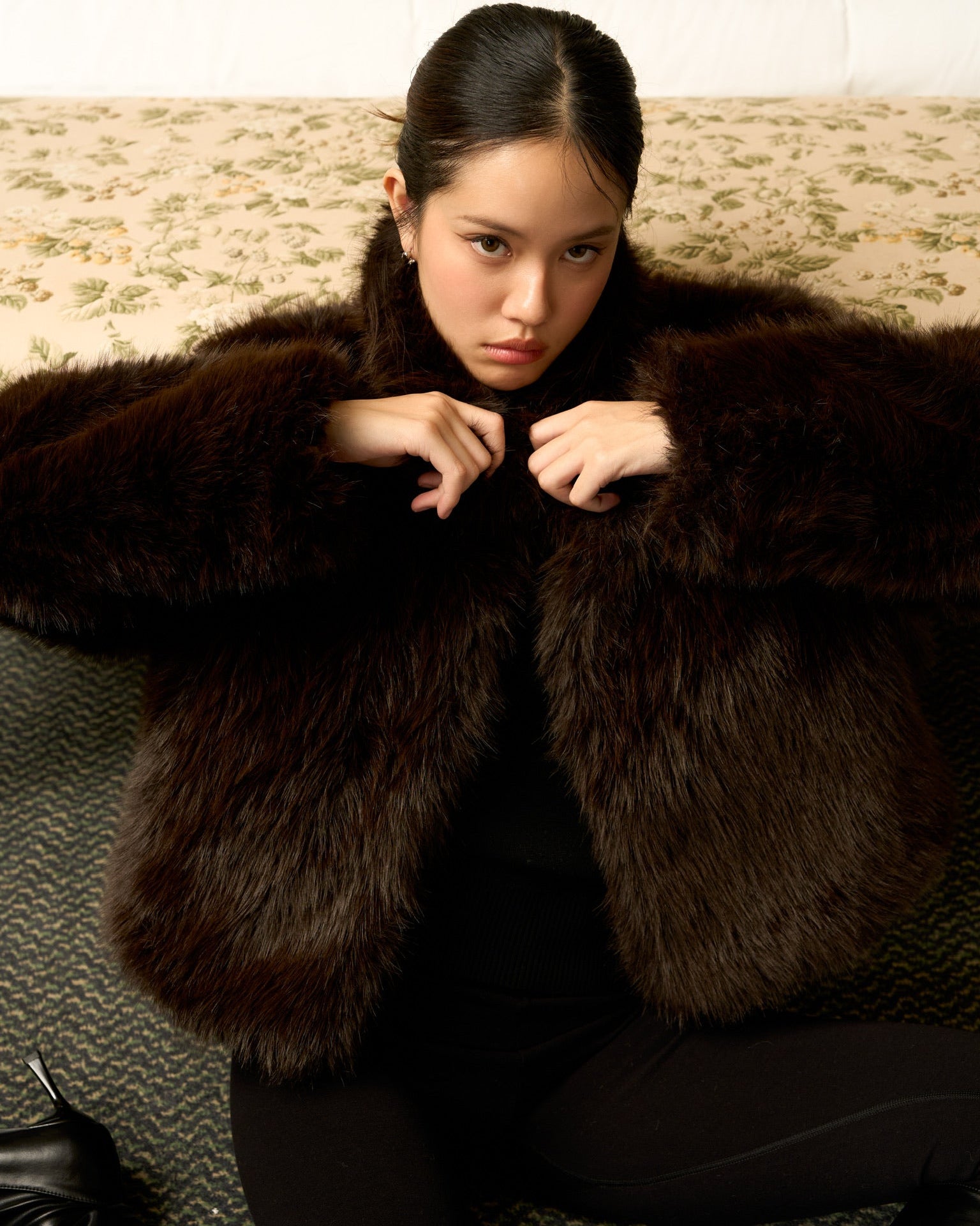 Woman wearing a dark brown fur coat sitting on a textured surface.