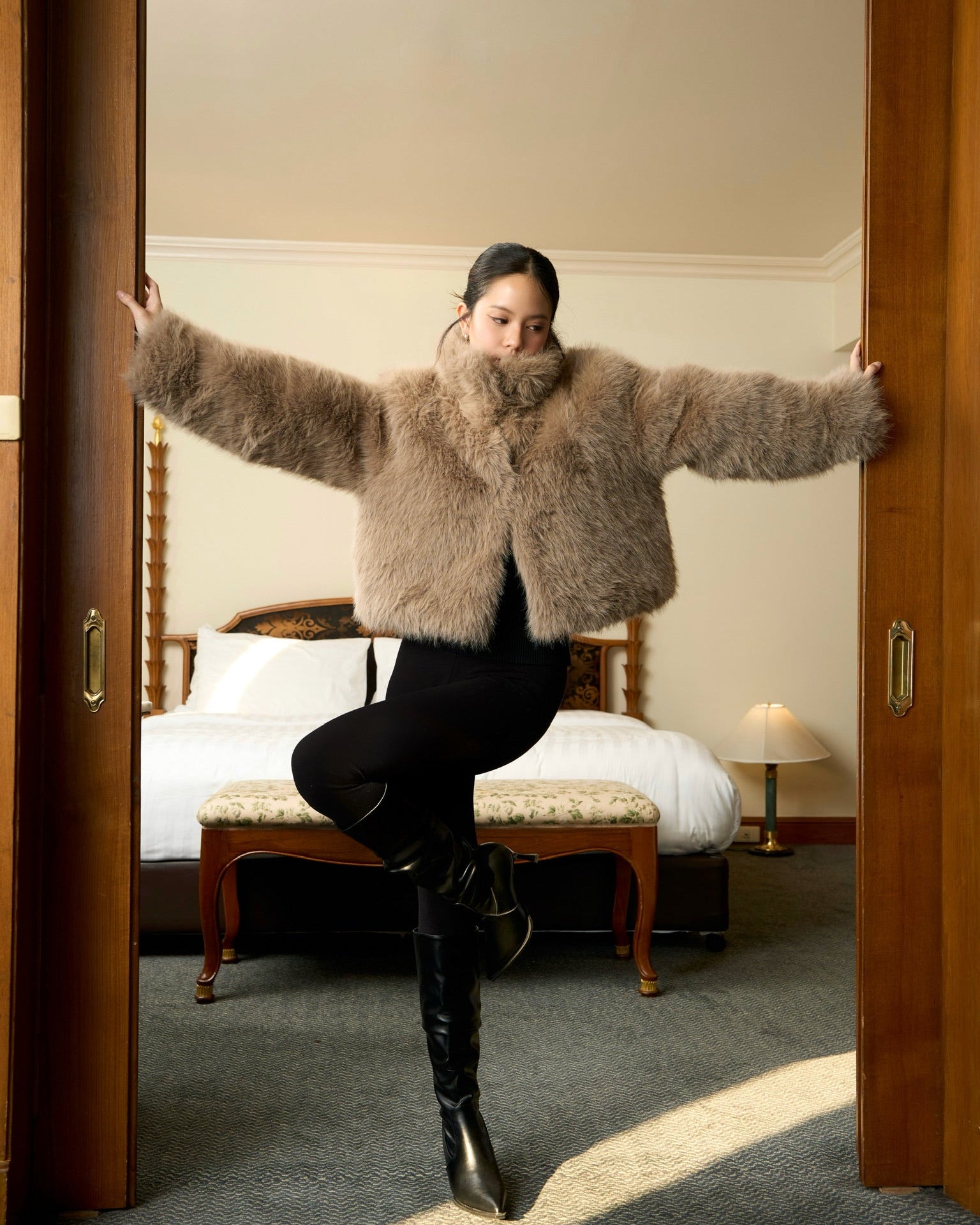 Woman wearing a mink fur coat and black boots in a bedroom setting