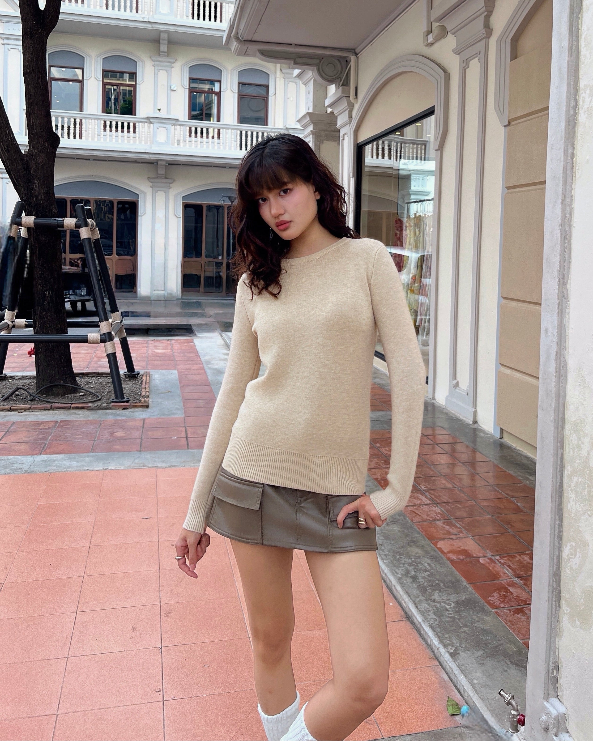Woman in a beige sweater and skirt standing in front of a building.