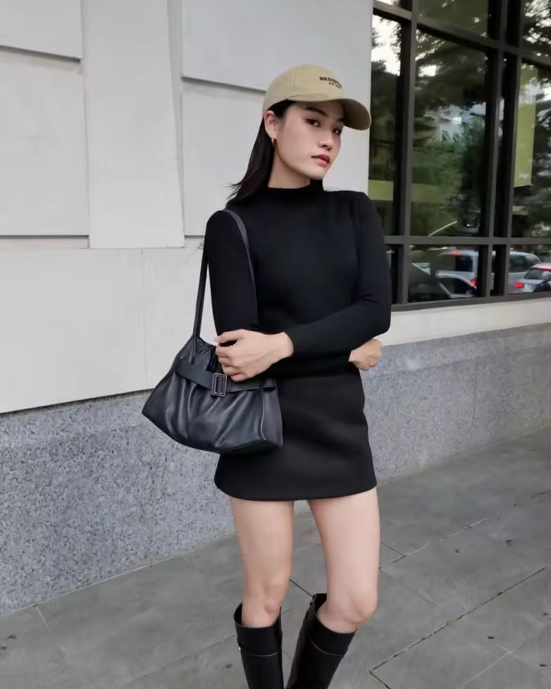 Woman in black outfit with a cap and boots standing outdoors.