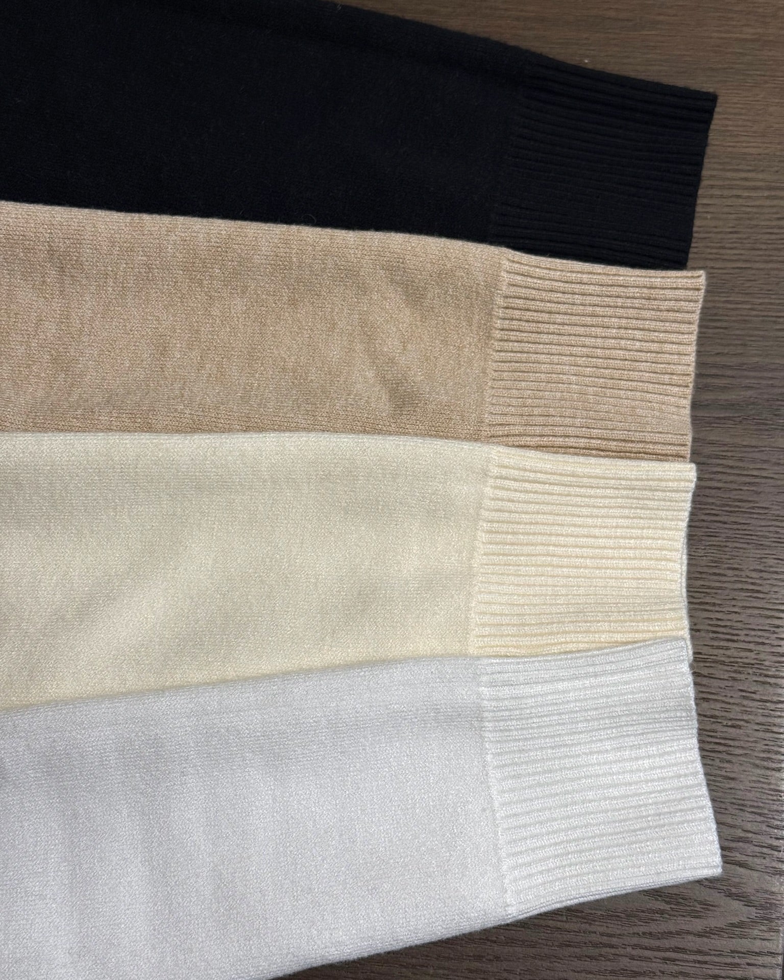 Close-up of a folded sweater with black, beige, and white sections on a wooden surface.