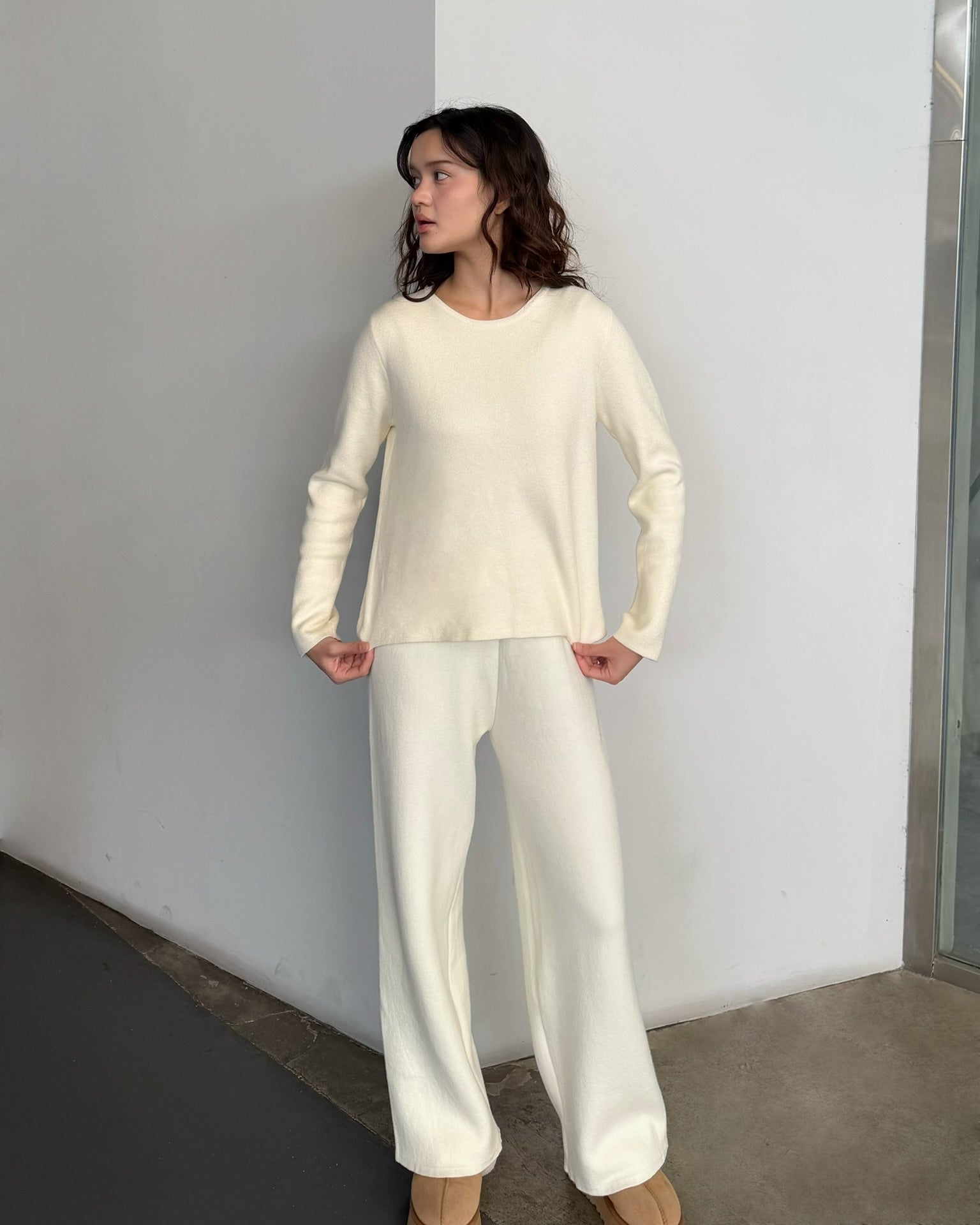 Woman wearing a cream-colored outfit against a plain wall.