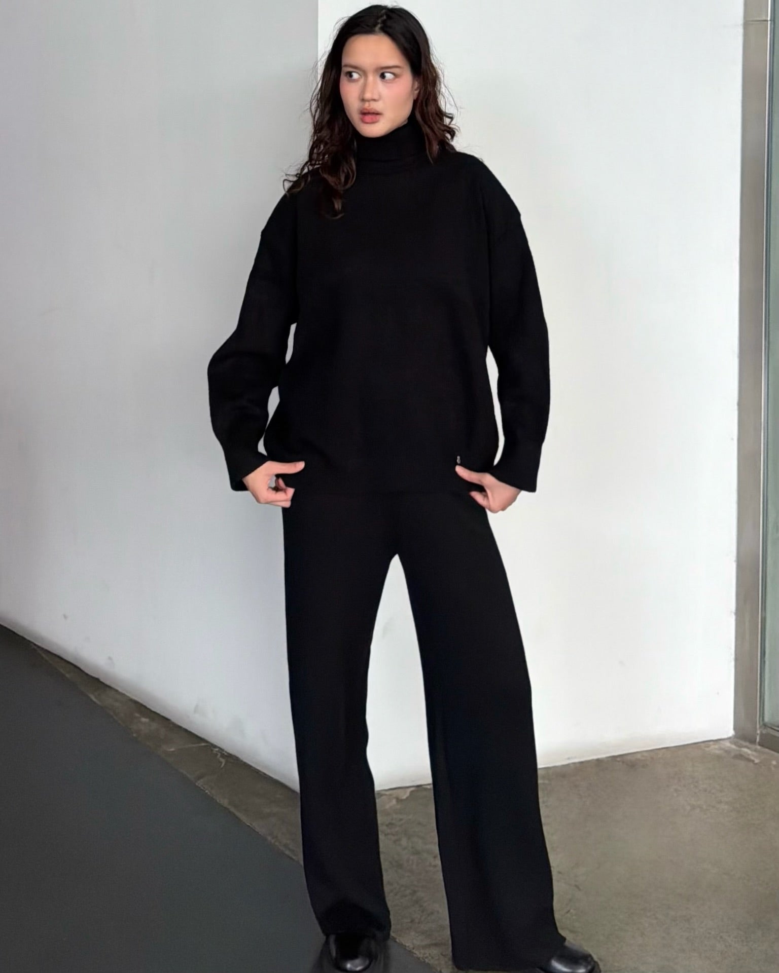 woman wearing a black outfit standing against a white wall.