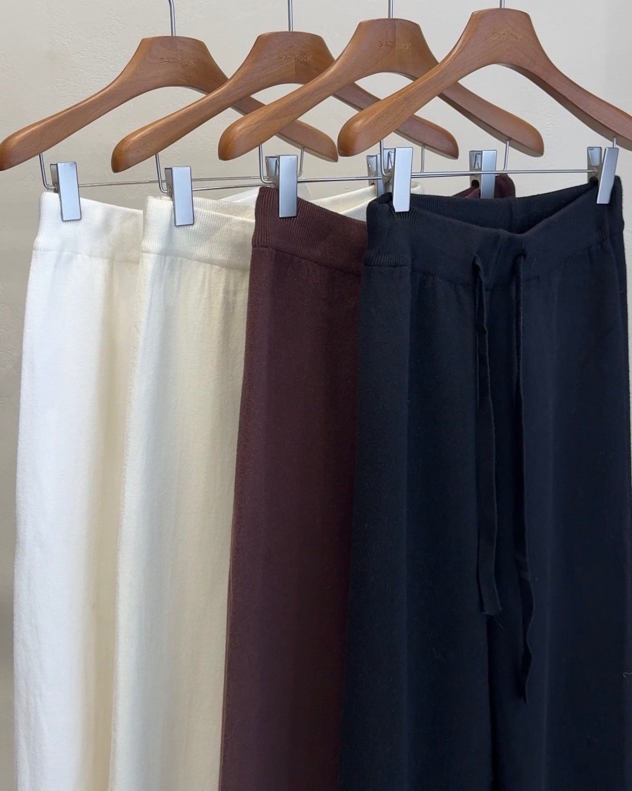 Three pairs of pants hanging on wooden hangers against a neutral background