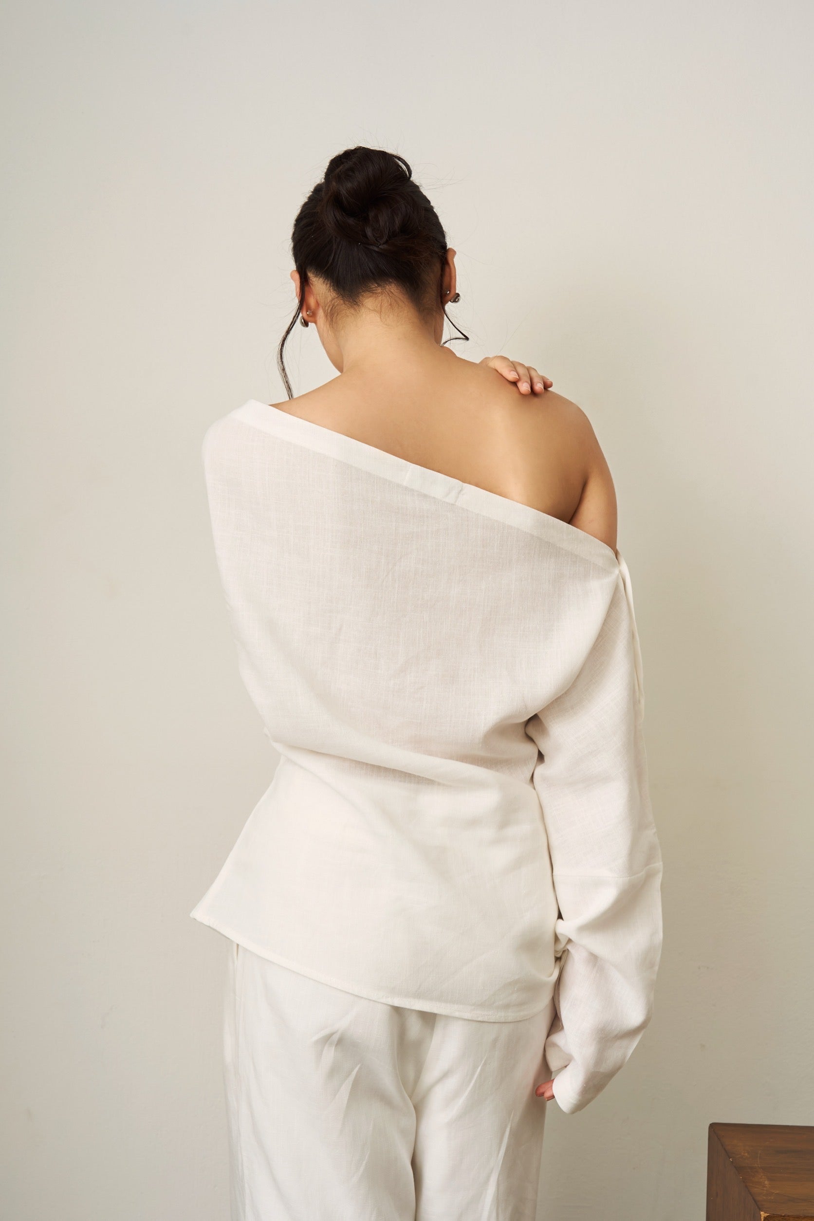 Back of a woman wearing a white off-shoulder linen top and pants against a plain background