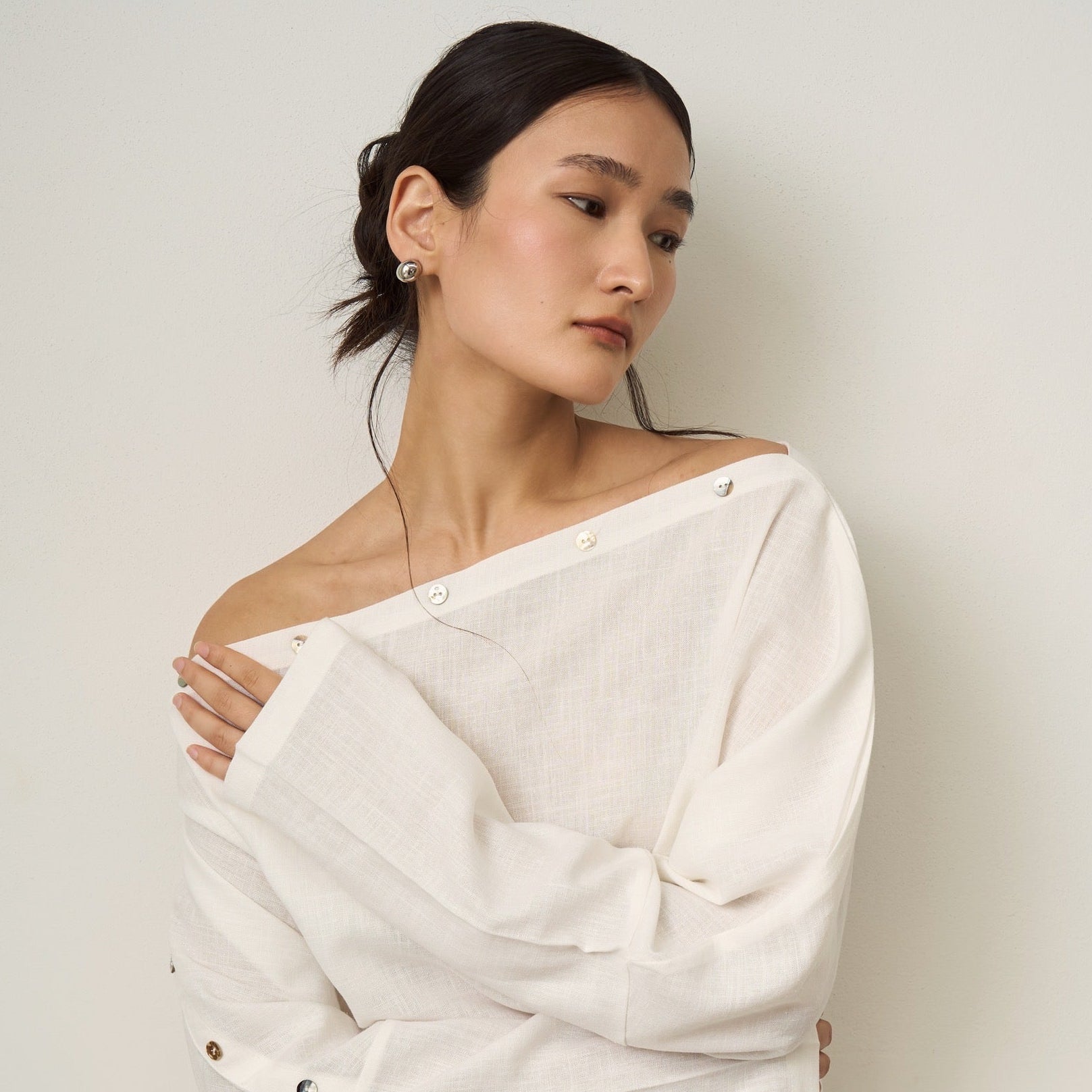 Close up of a woman wearing a white off-shoulder top against a plain background.