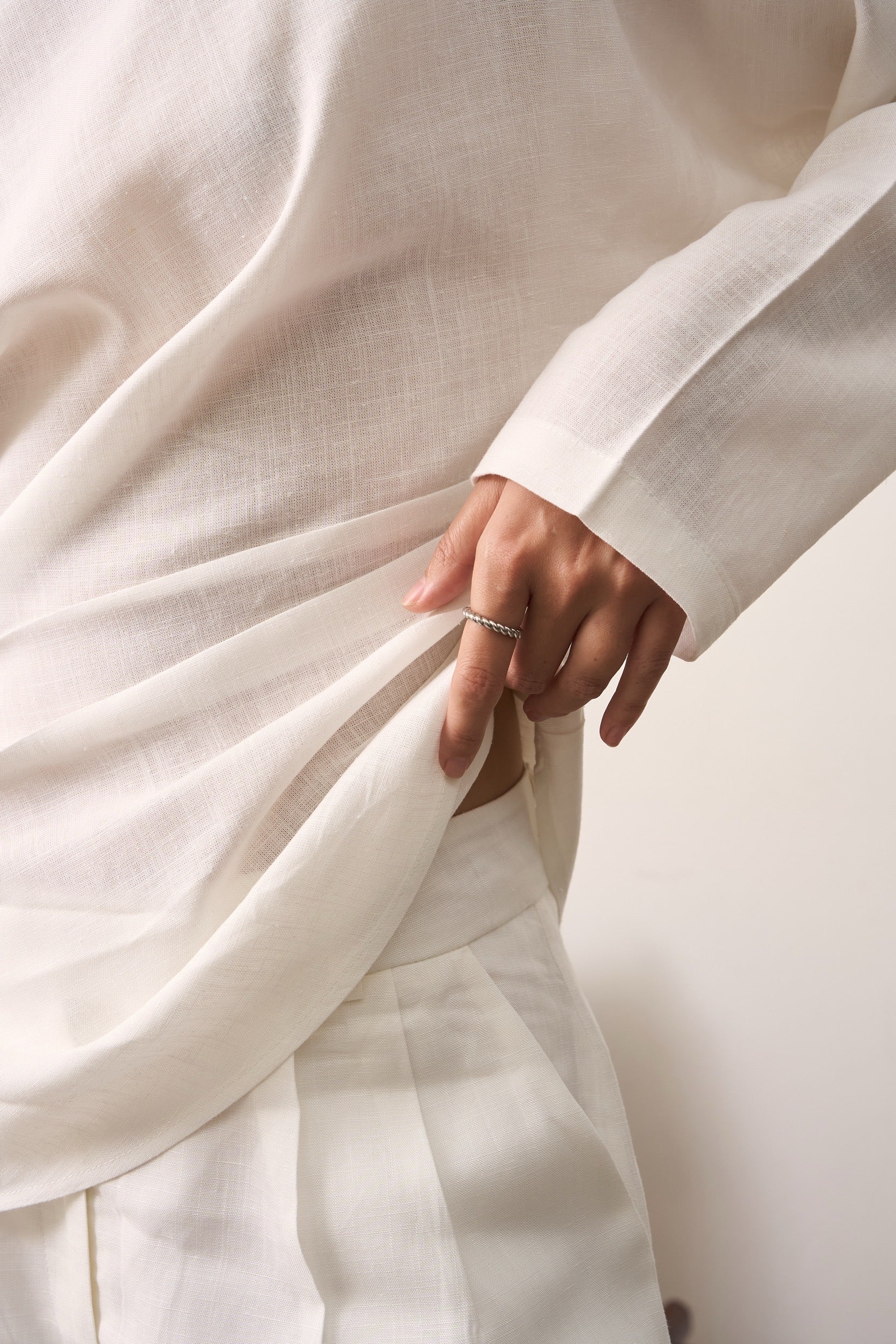 Close-up of a hand holding white linen fabric showing linen shirt and linen pants with a blurred background