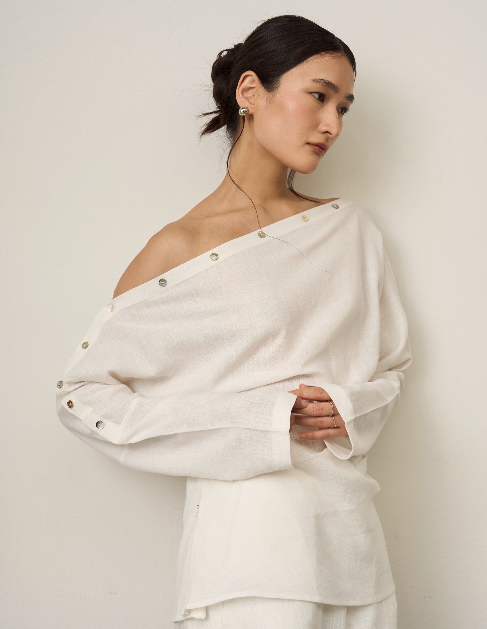 Woman wearing a white off-shoulder linen shirt with button details against a plain background