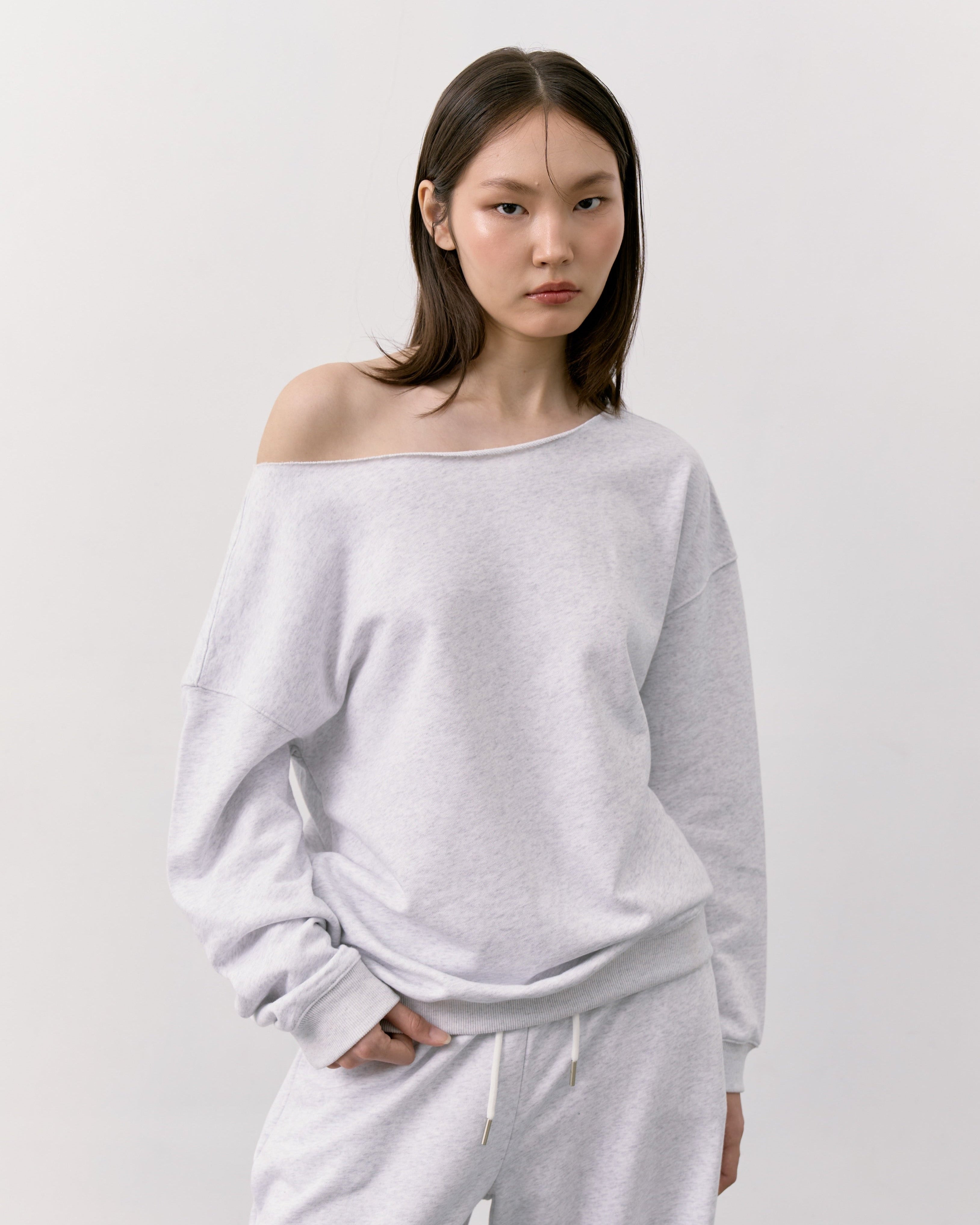 Woman wearing a light gray off-shoulder top and pants on a white background
