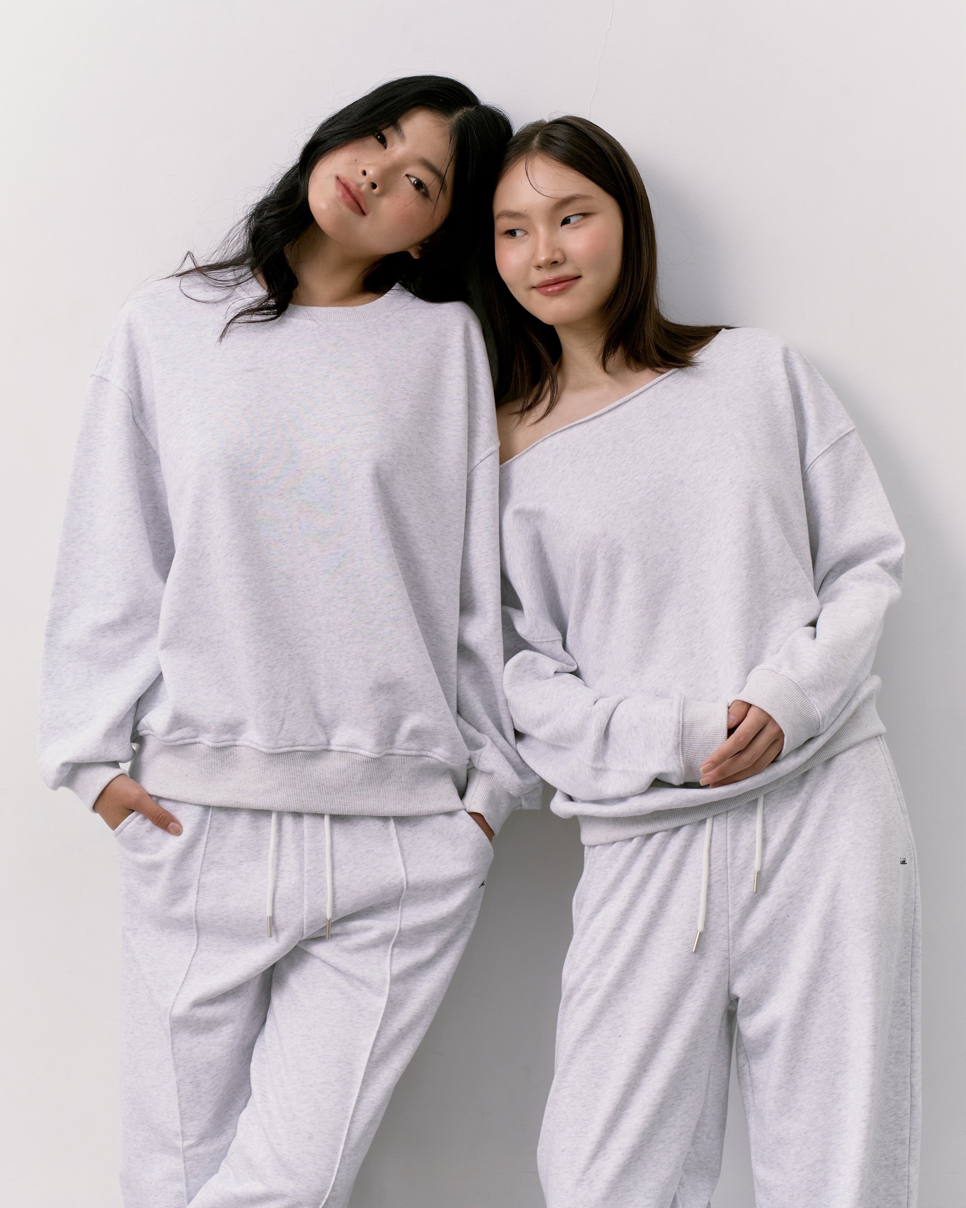 Two women wearing matching light gray sweatshirts and pants against a white background