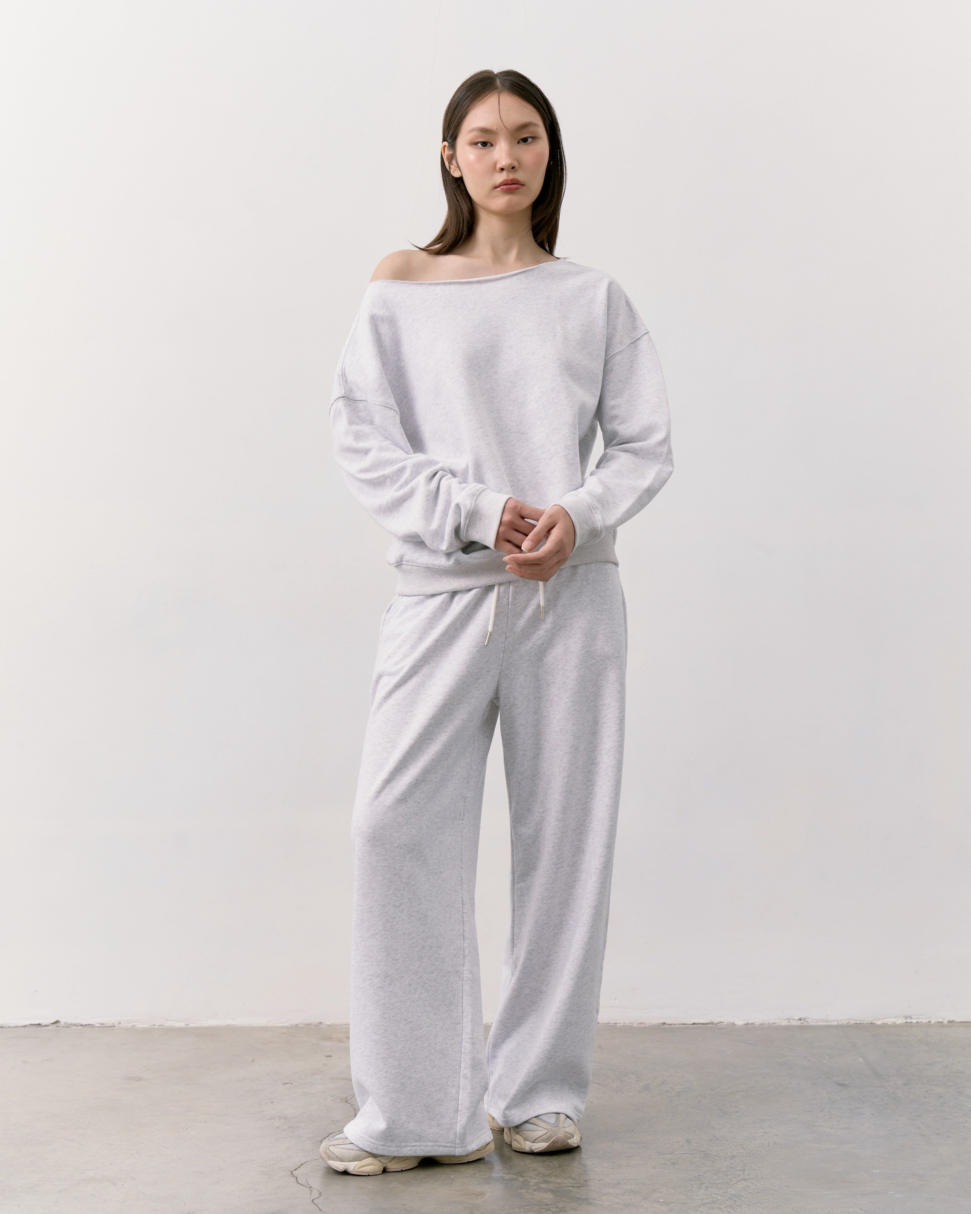 woman wearing a white off-shoulder top and wide-leg pants against a plain background