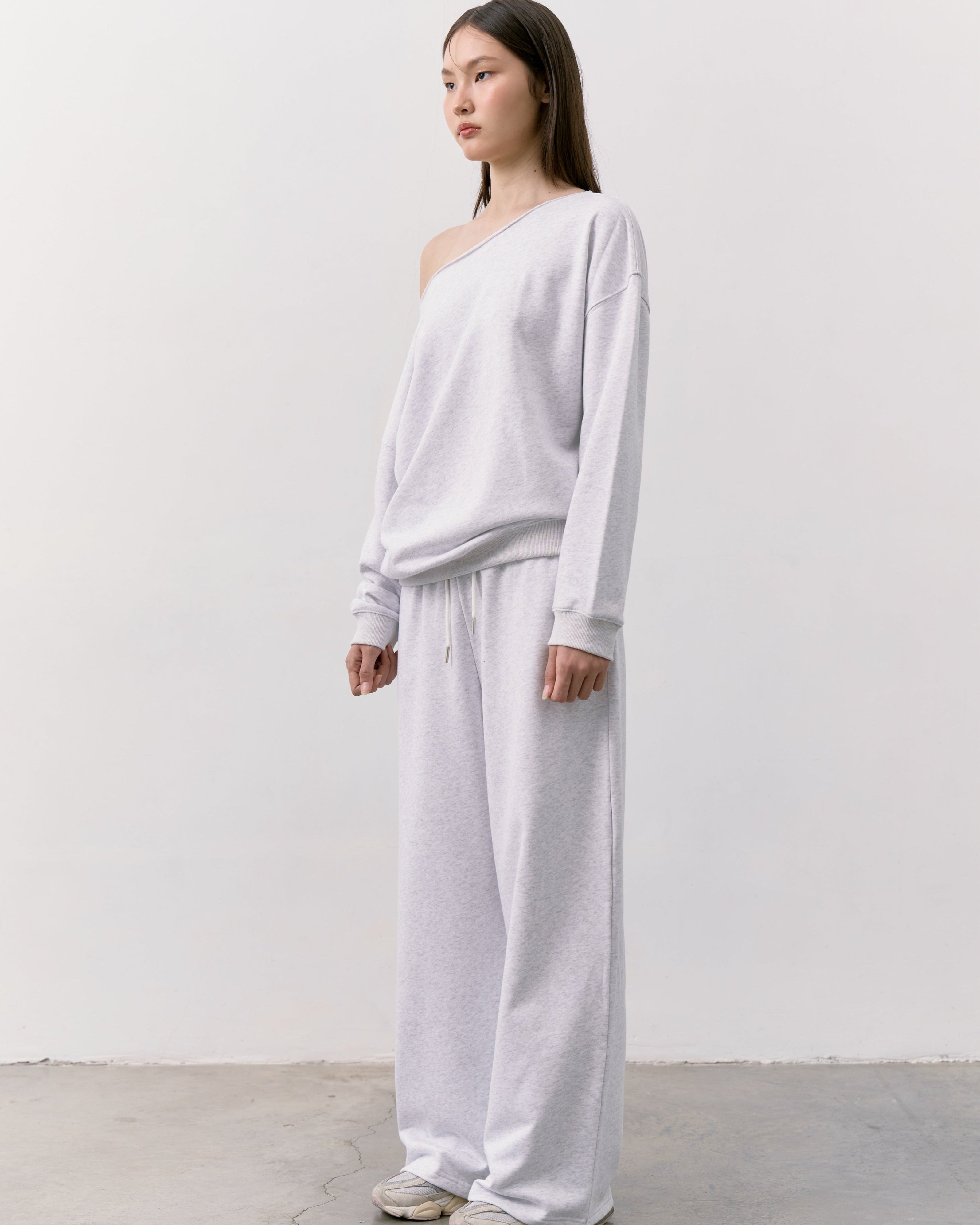 woman wearing a white one-shoulder top and pants against a plain background