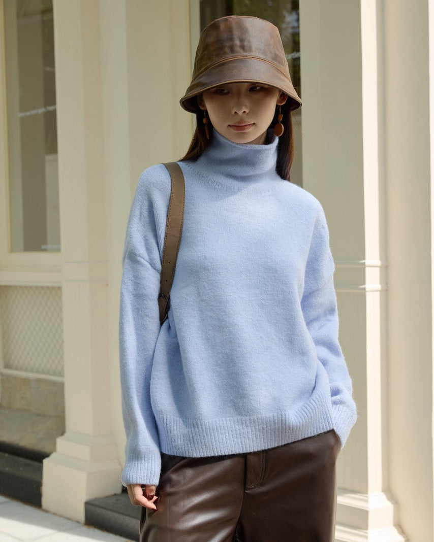 woman wearing a light blue sweater and brown bucket hat standing outdoors.