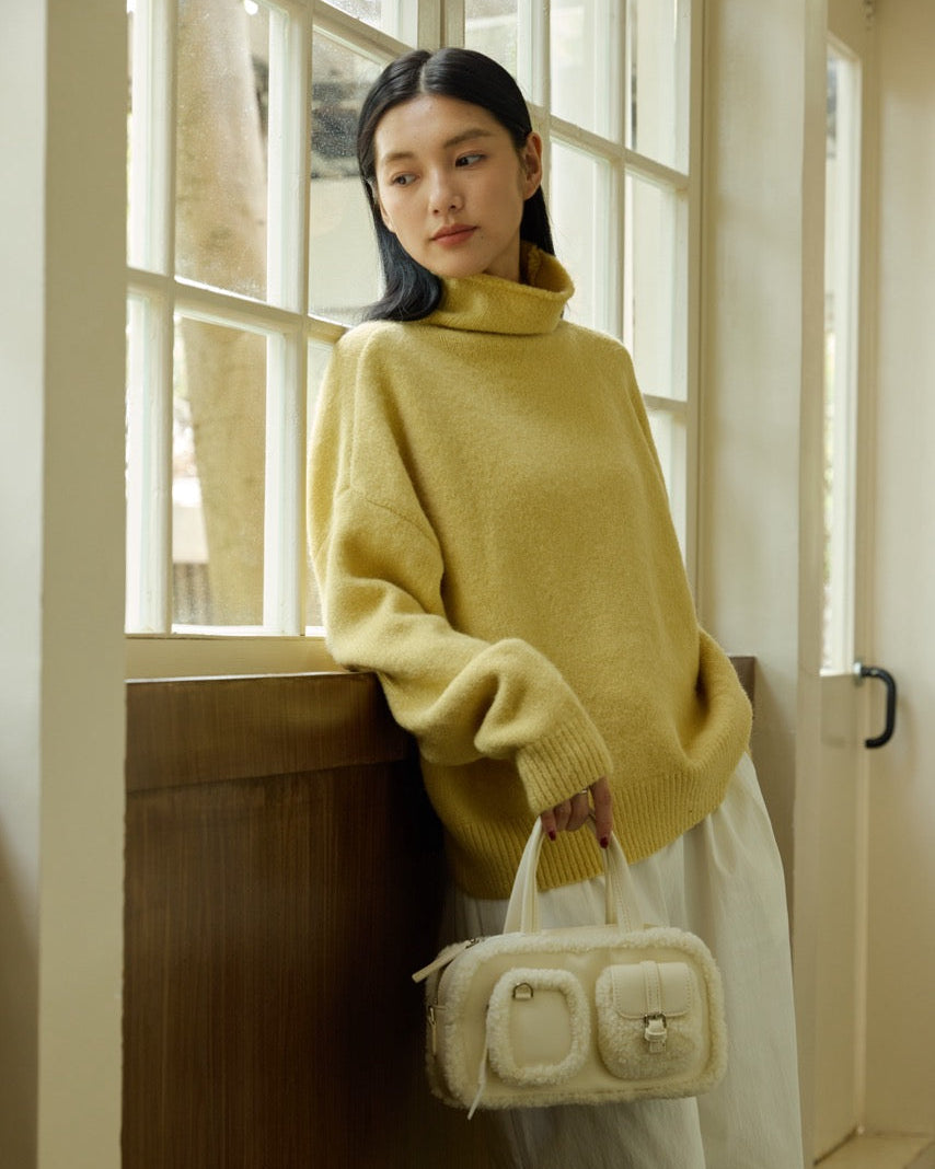 Woman in a yellow sweater holding a white handbag by a window
