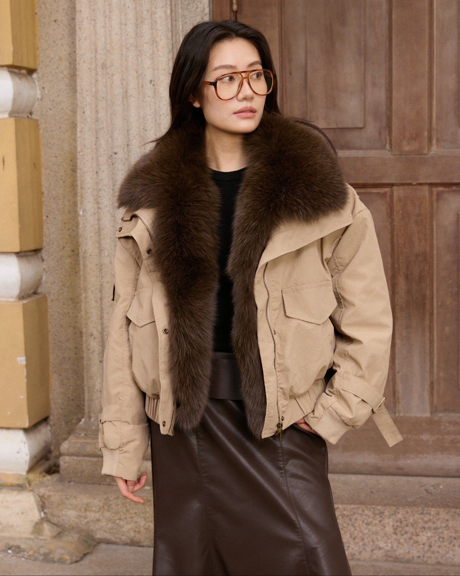 Woman wearing a beige jacket with fur collar standing in front of a wooden door.