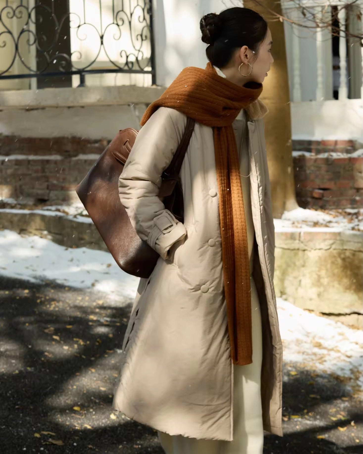 Person wearing a long coat and orange scarf in a snowy outdoor setting