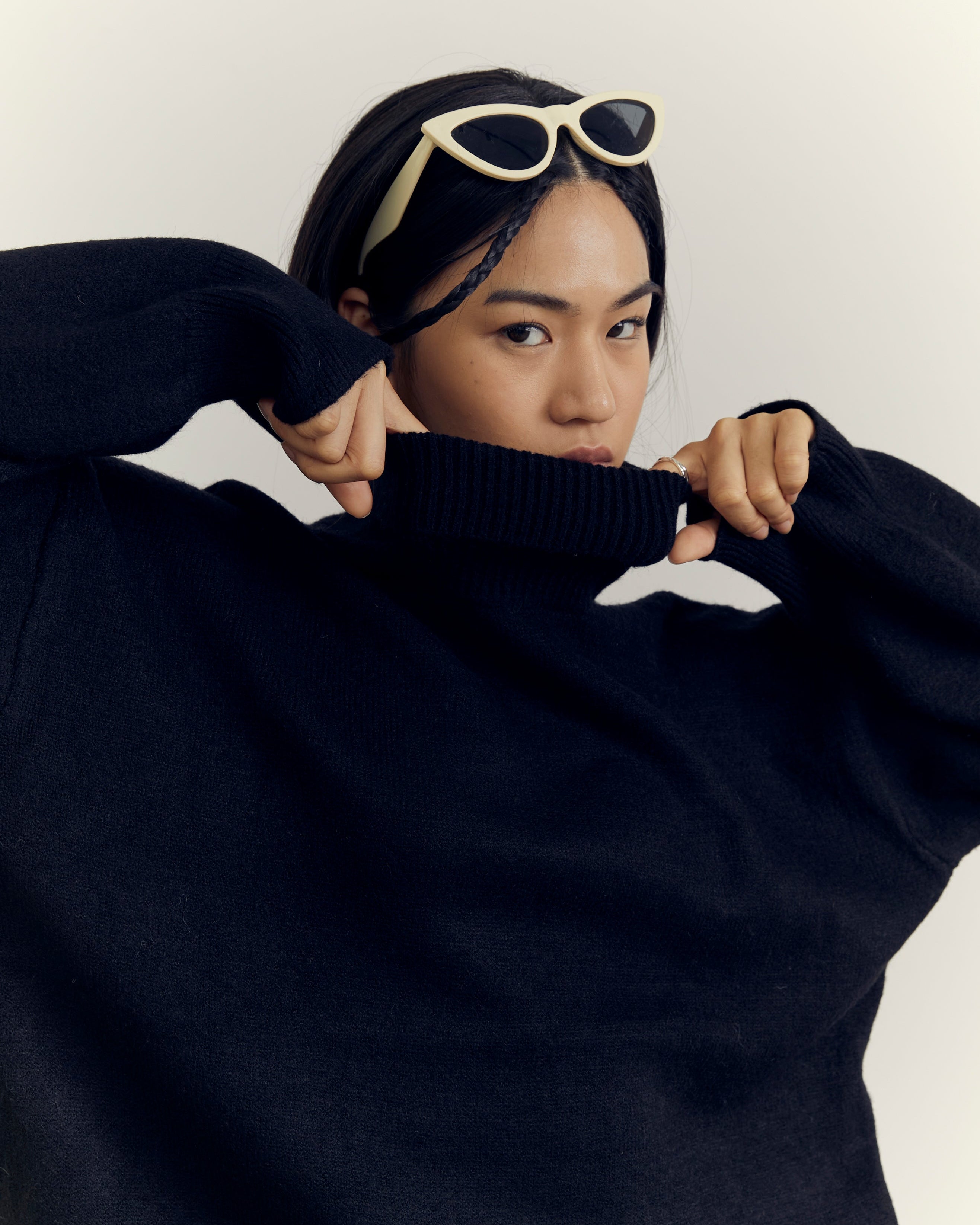 Person wearing a black sweater with a white logo on a plain background