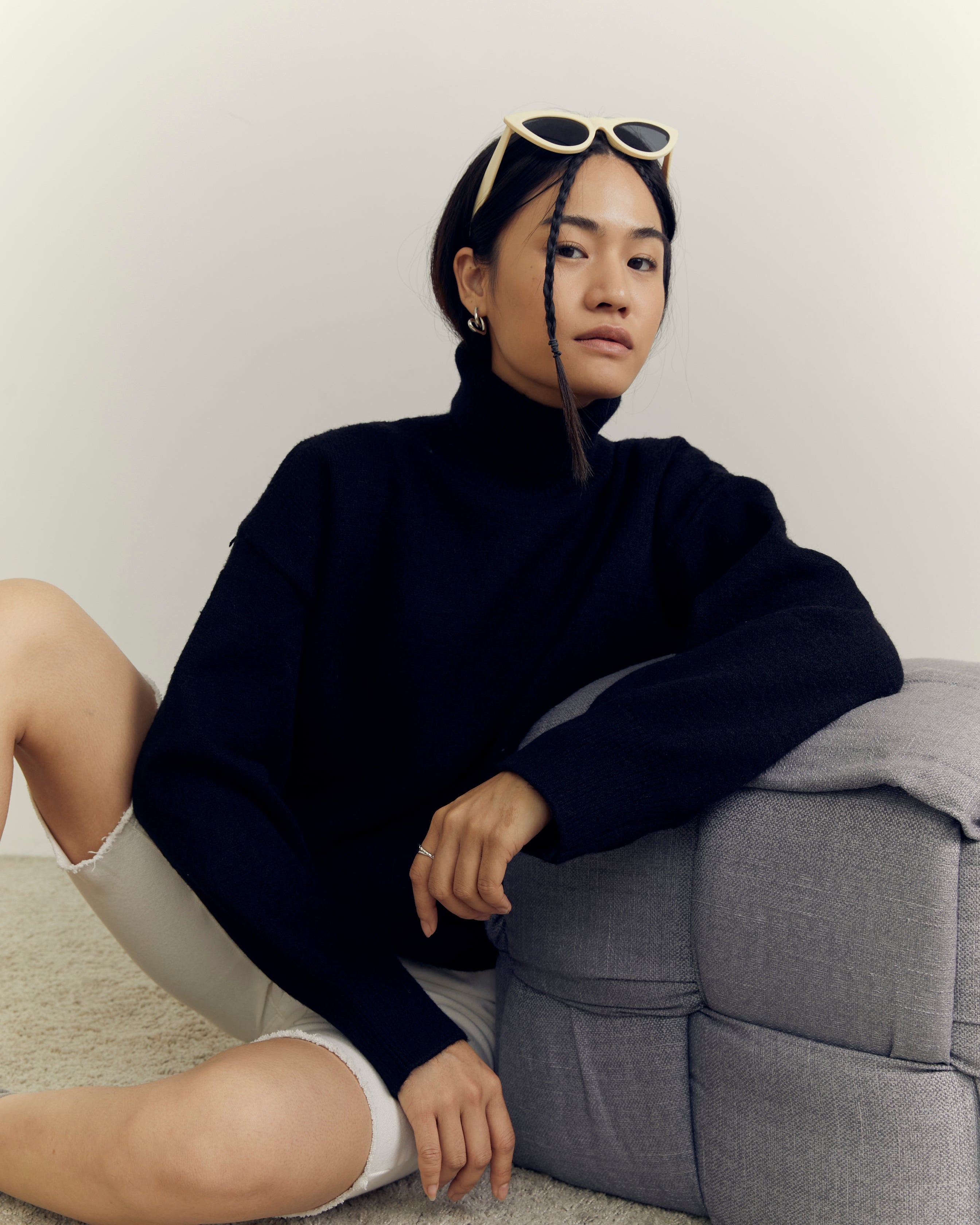 Person sitting on a gray chair wearing a dark sweater and white pants.
