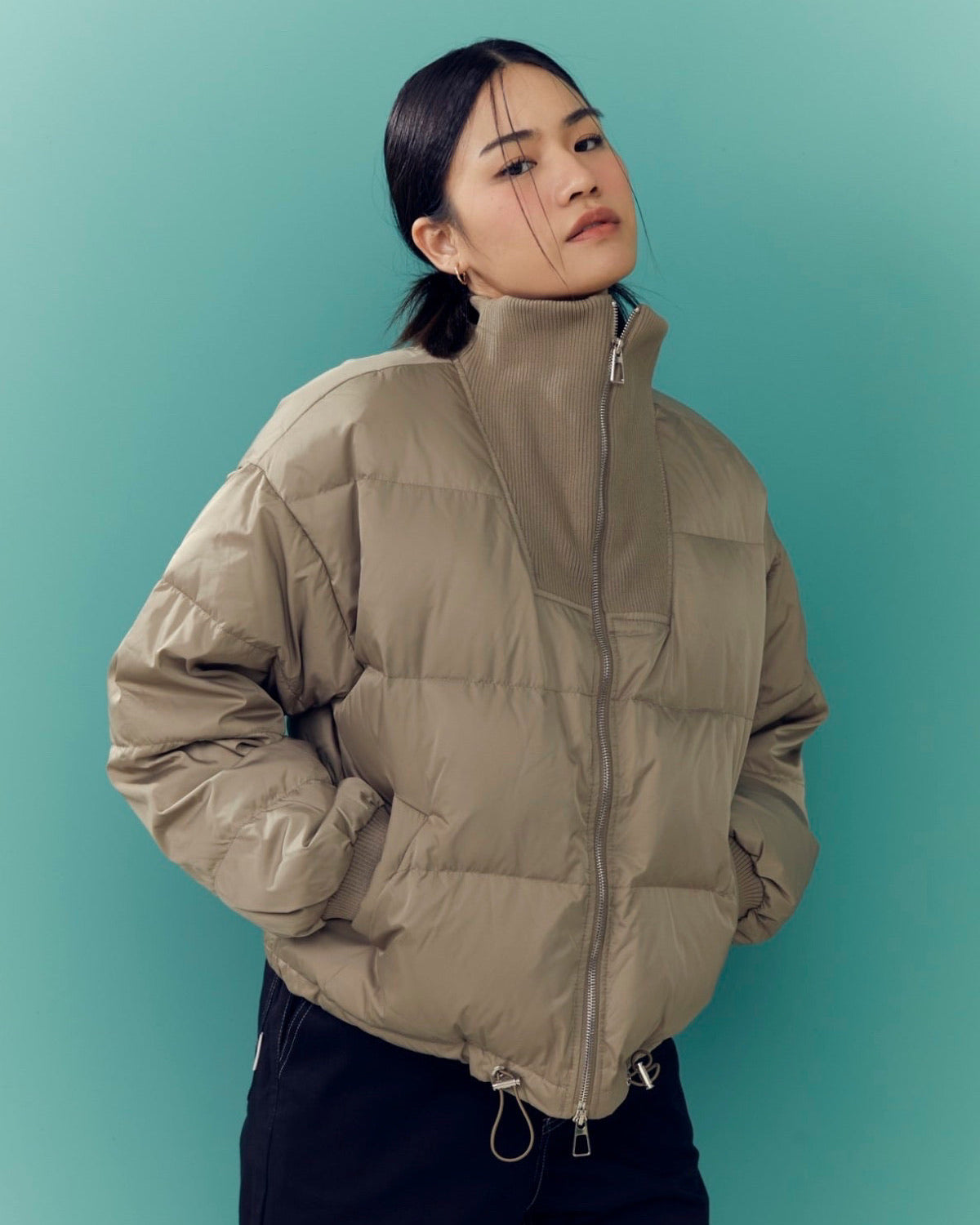 woman wearing a beige puffer jacket against a teal background
