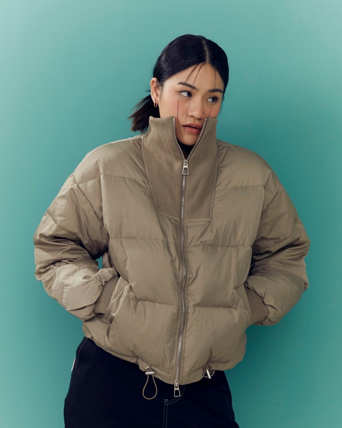 woman wearing a beige puffer jacket against a teal background
