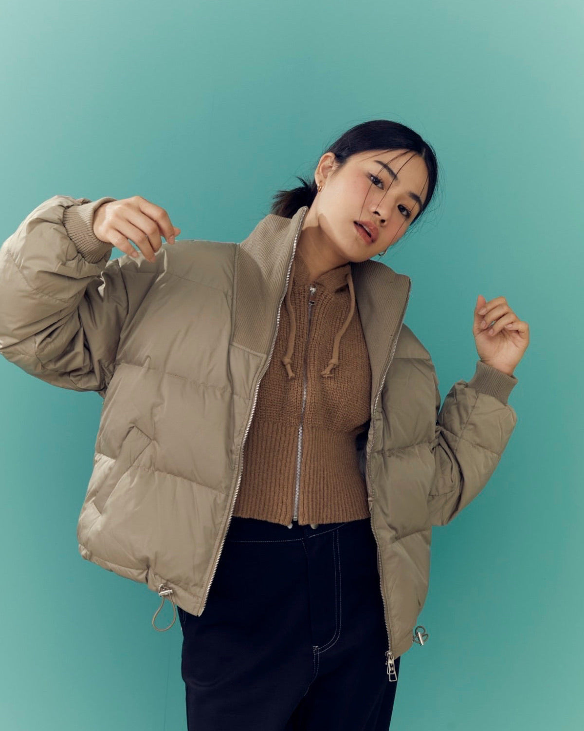 woman wearing a beige puffer jacket against a teal background