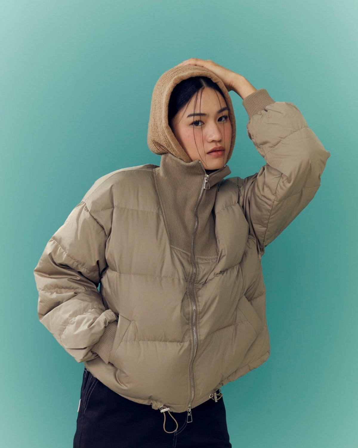 woman wearing a beige puffer jacket against a teal background