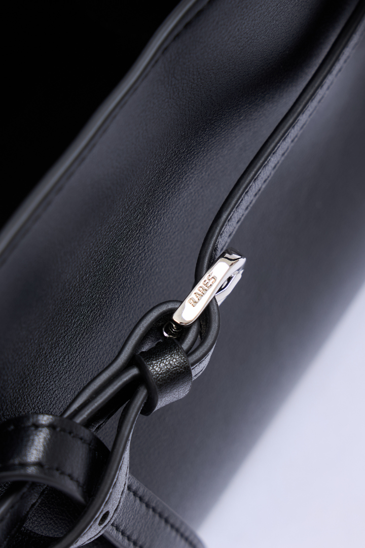 Close-up of a black leather handbag with a silver-tone metal zipper pull engraved with the brand name 'LUMIÈRE'.