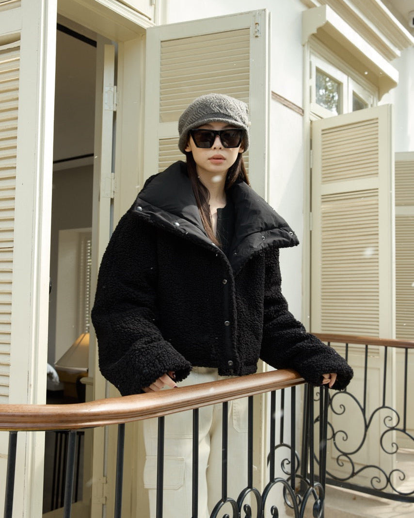 woman wearing a black coat and sunglasses standing on a balcony.