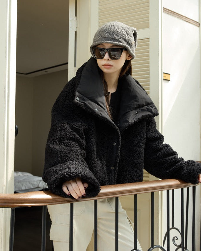 woman wearing a black coat, gray beanie, and sunglasses on a balcony.