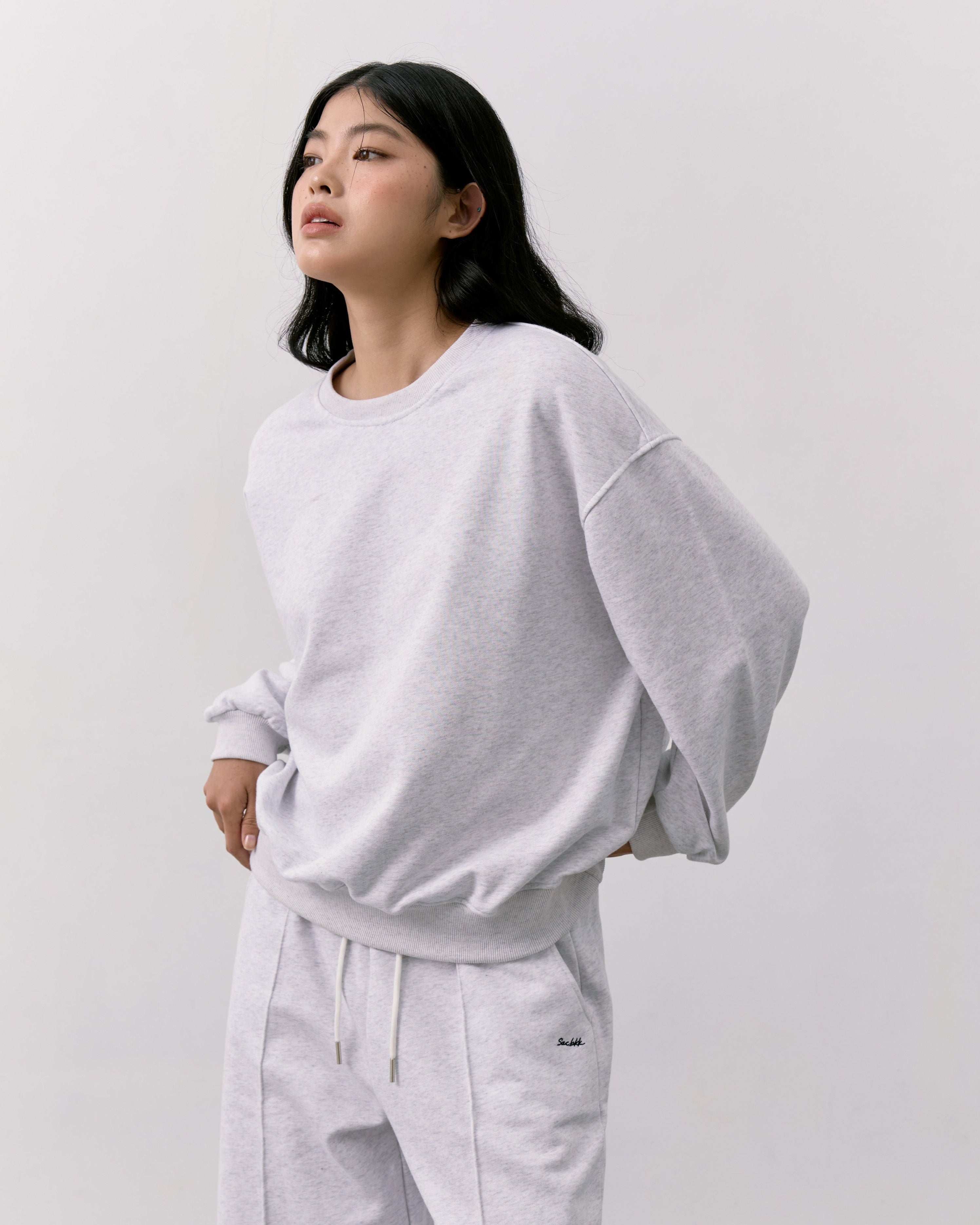 woman wearing a light gray oversized sweatshirt and white pants against a plain background
